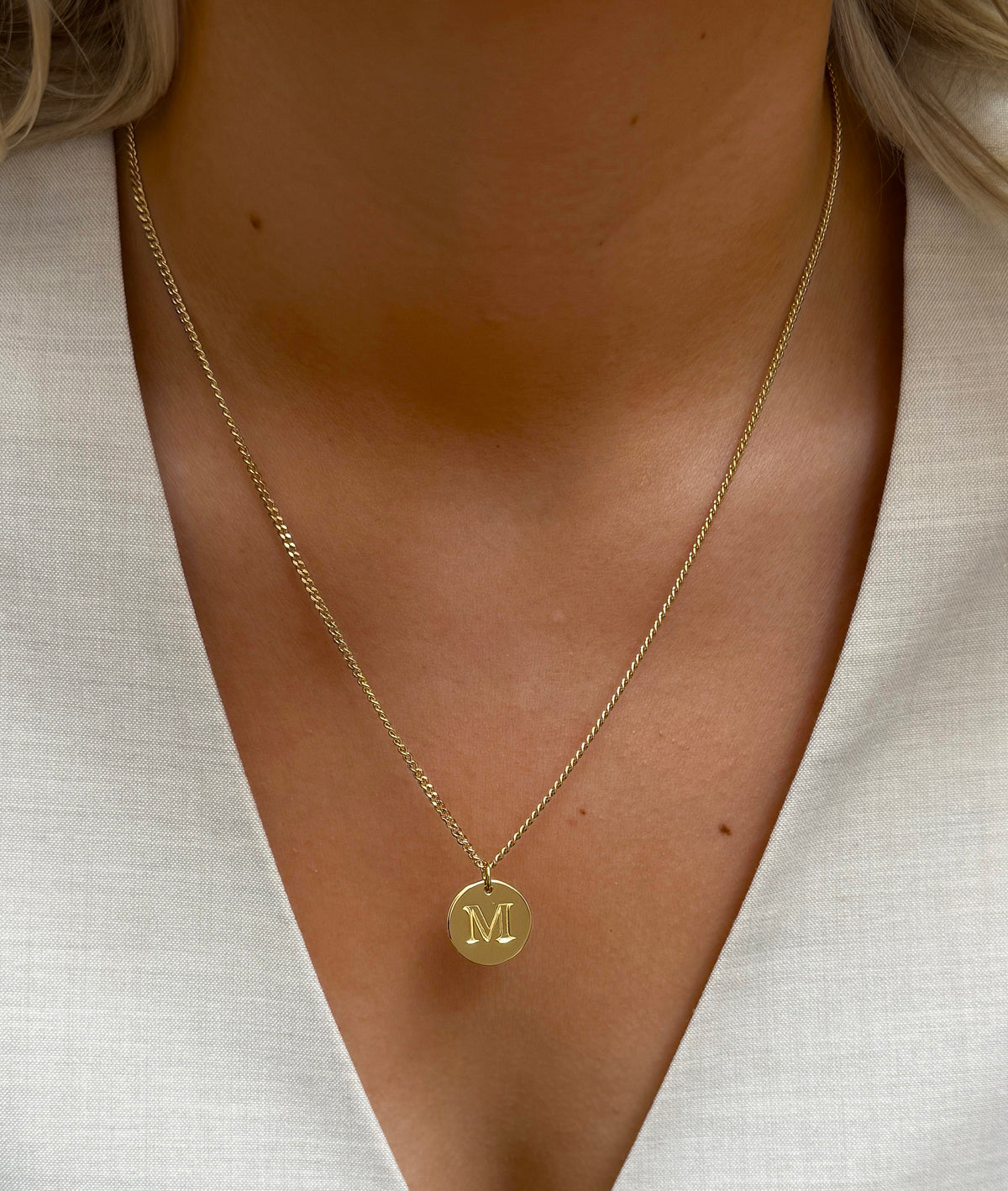 A close-up shot of a model wearing the Beloved Big Letter 'M' charm in gold, paired with a matching gold curb chain necklace.