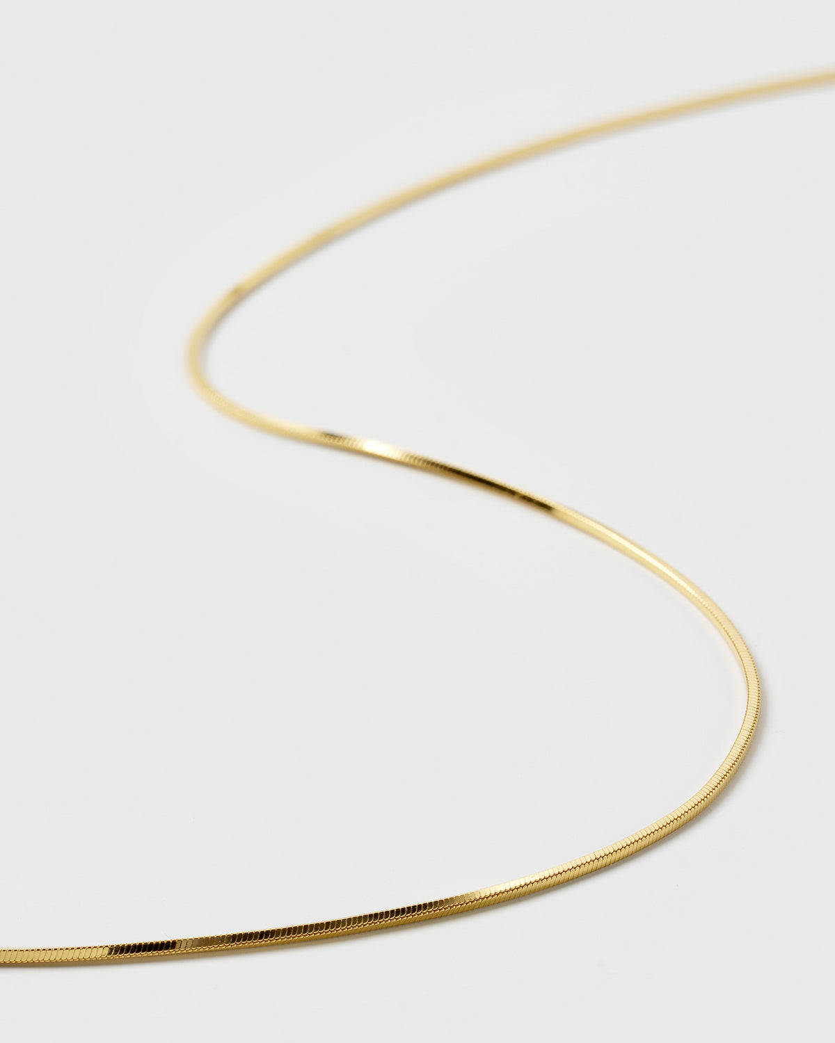 A close-up product shot of the Sheer Mirror Necklace Gold, showcasing its smooth and reflective flat chain design.