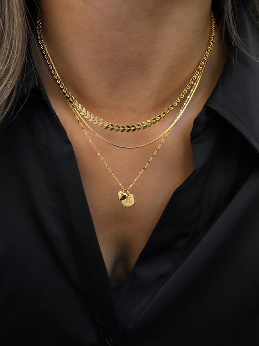 Three gold necklaces side by side, a gold necklace with hearts and spikes, a gold necklace with a combination of two different types of chains, and a gold necklace with elegant freshwater pearls.