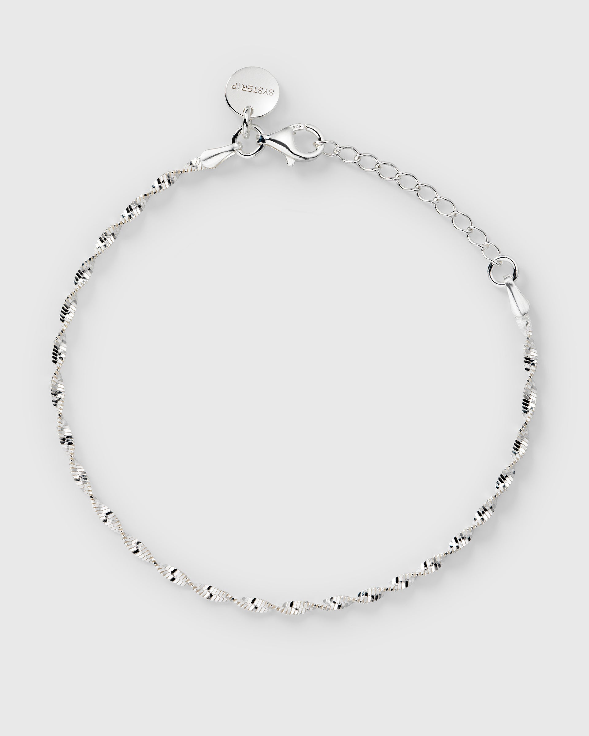 A product shot of the Advent Calendar Door 10 twisted herringbone bracelet in silver, laid out in a circle to display its delicate chain, clasp, and Syster P tag.