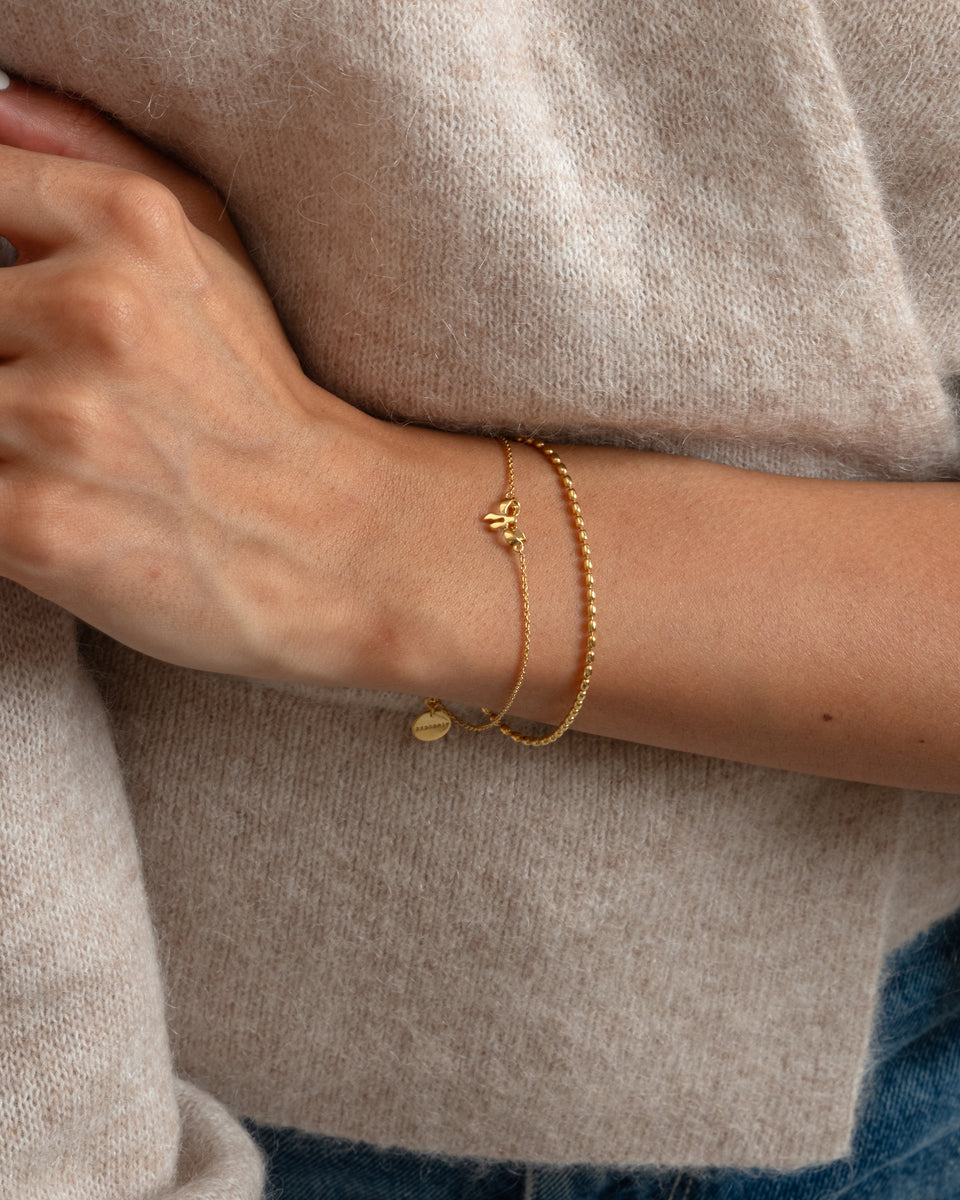 A close-up of a model's wrist wearing the Lunetta Bracelet in gold, featuring a ball chain with delicate oval beads.
