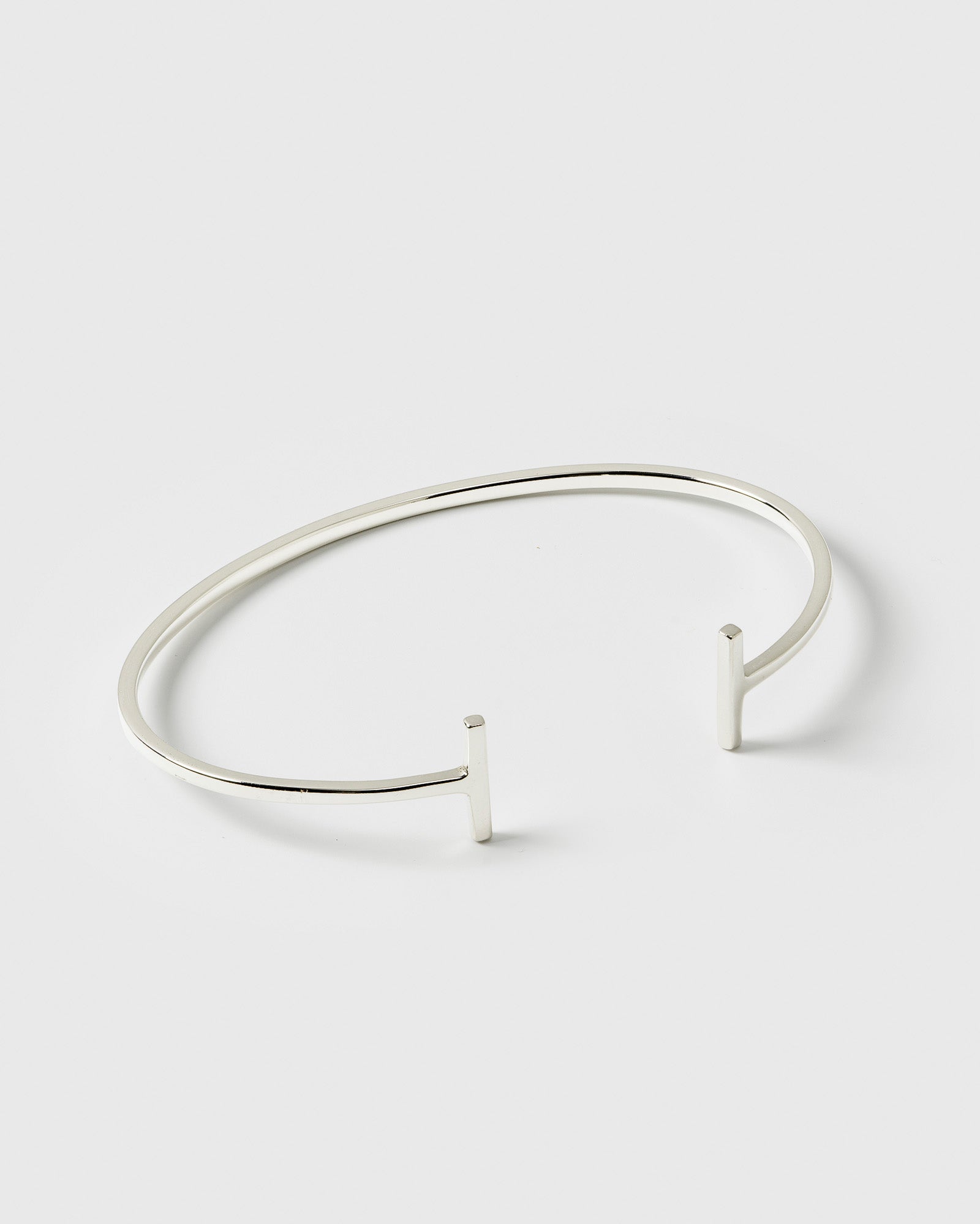 A product shot of the Strict Bar Bangle in silver, showing its thin, open design with a geometric bar at each end.