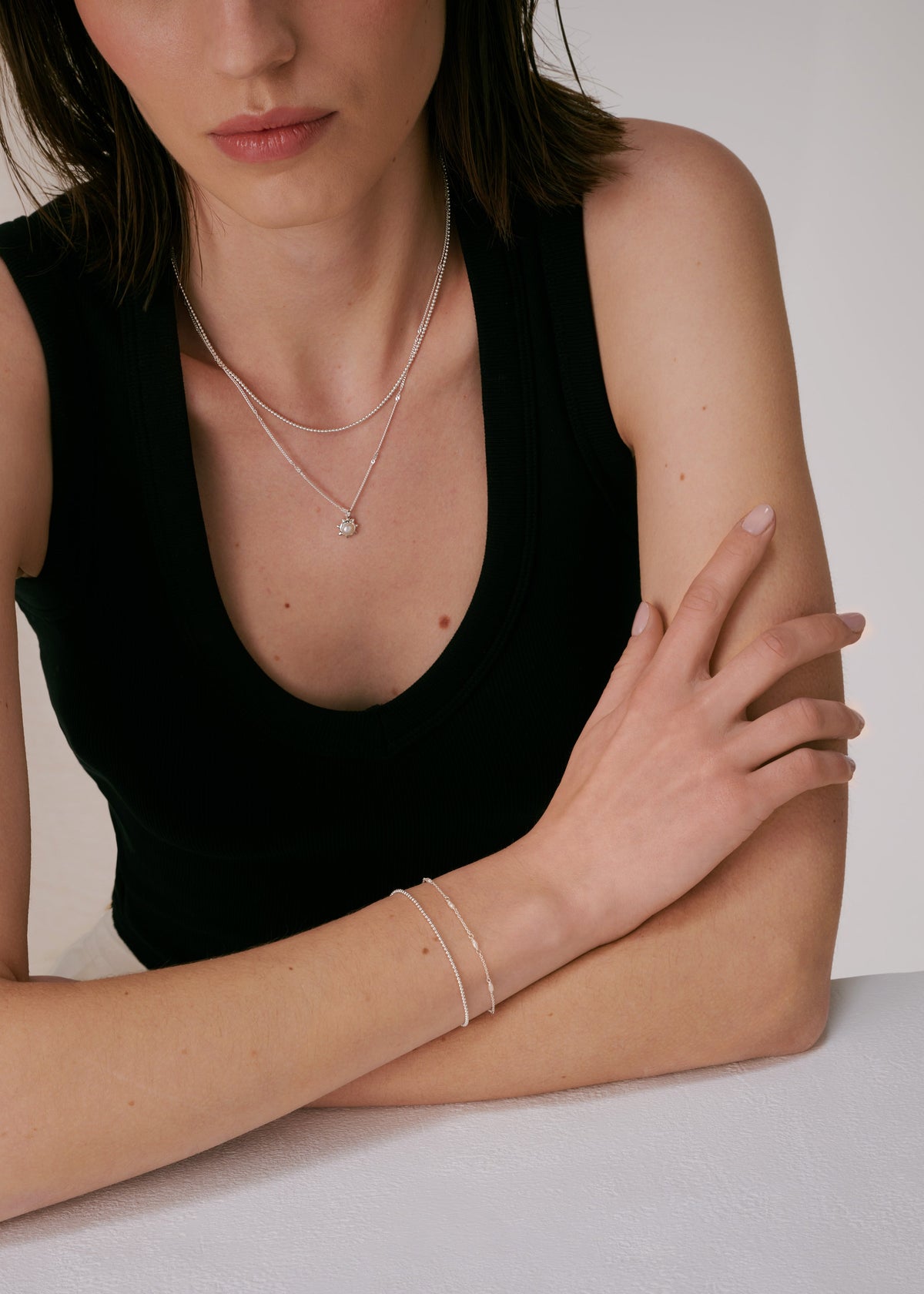 A silver bracelet with multiple freshwater pearls, layered with a simple silver chain bracelet, paired with a layered silver necklace featuring a freshwater pearl pendant.