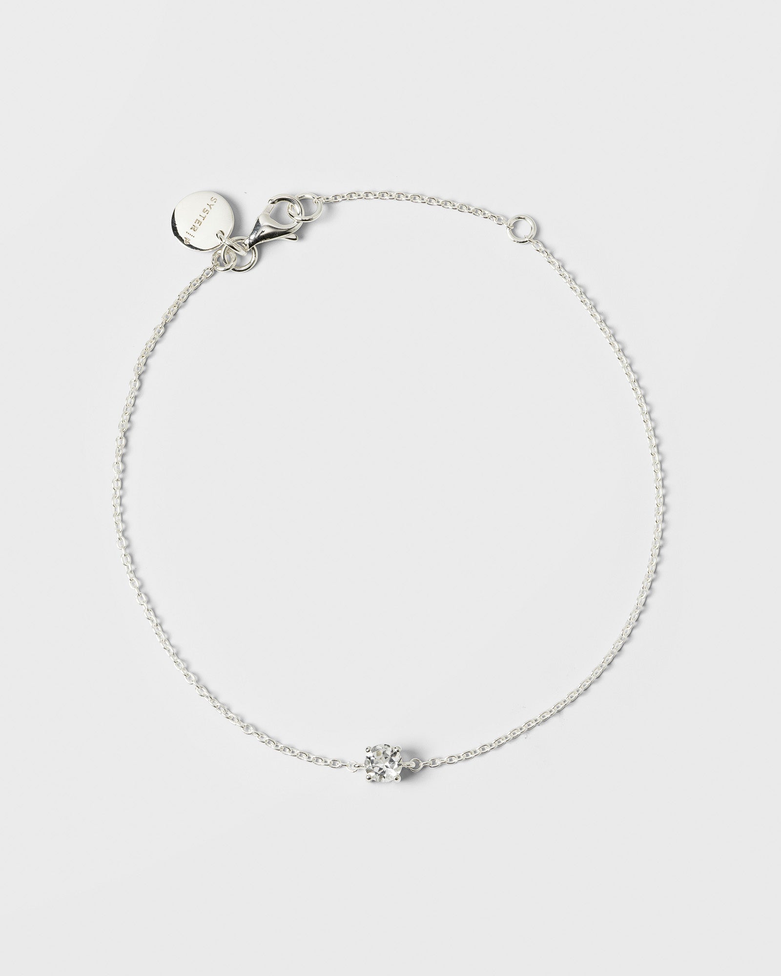 A product shot of the Minimalistica Solo Nova Bracelet in silver, laid out in a circle to show its design of a delicate chain with a single, central white topaz stone.
