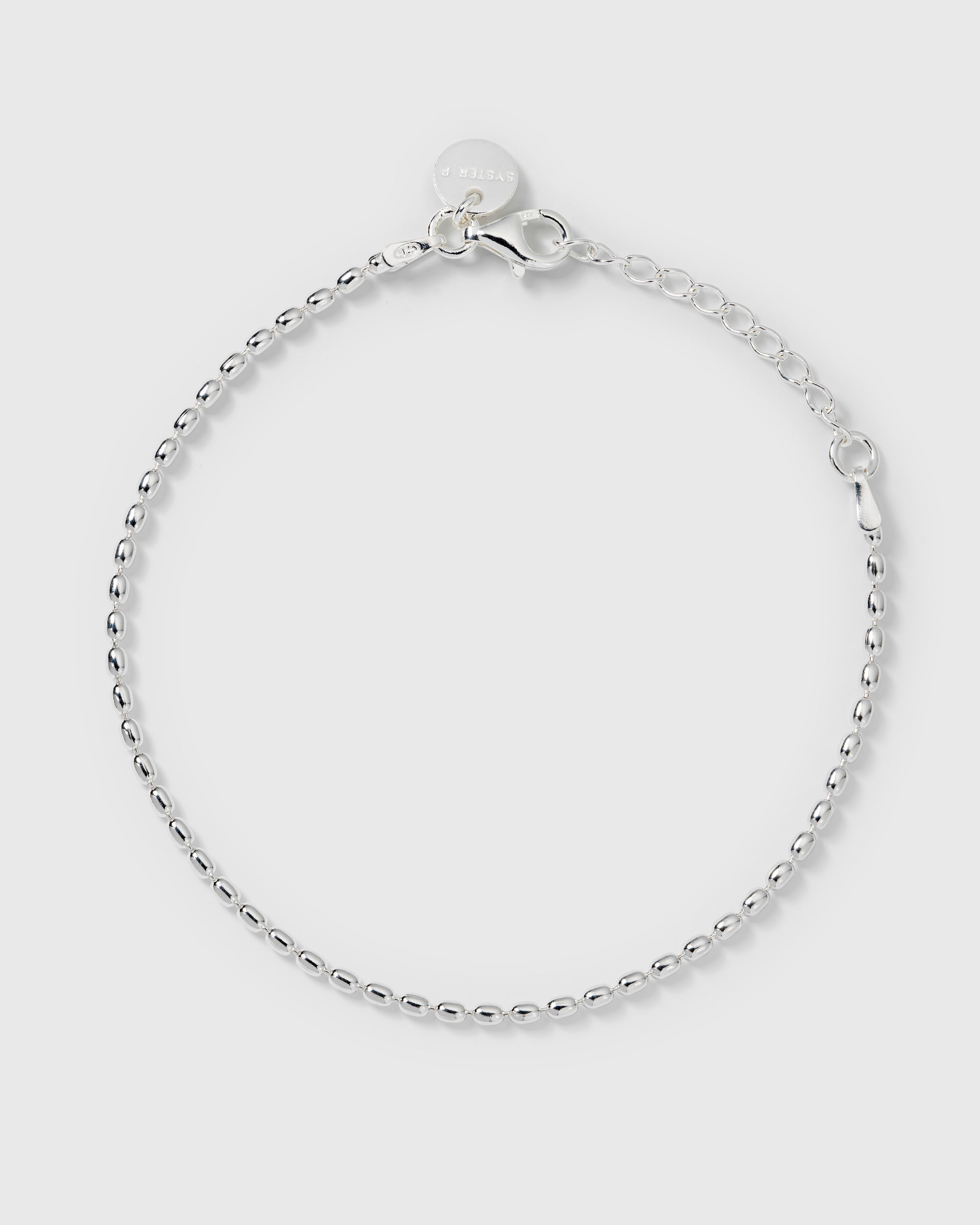 A product shot of the Lunetta Bracelet in silver, laid out in a circle to display its delicate chain made of small, elongated beads.