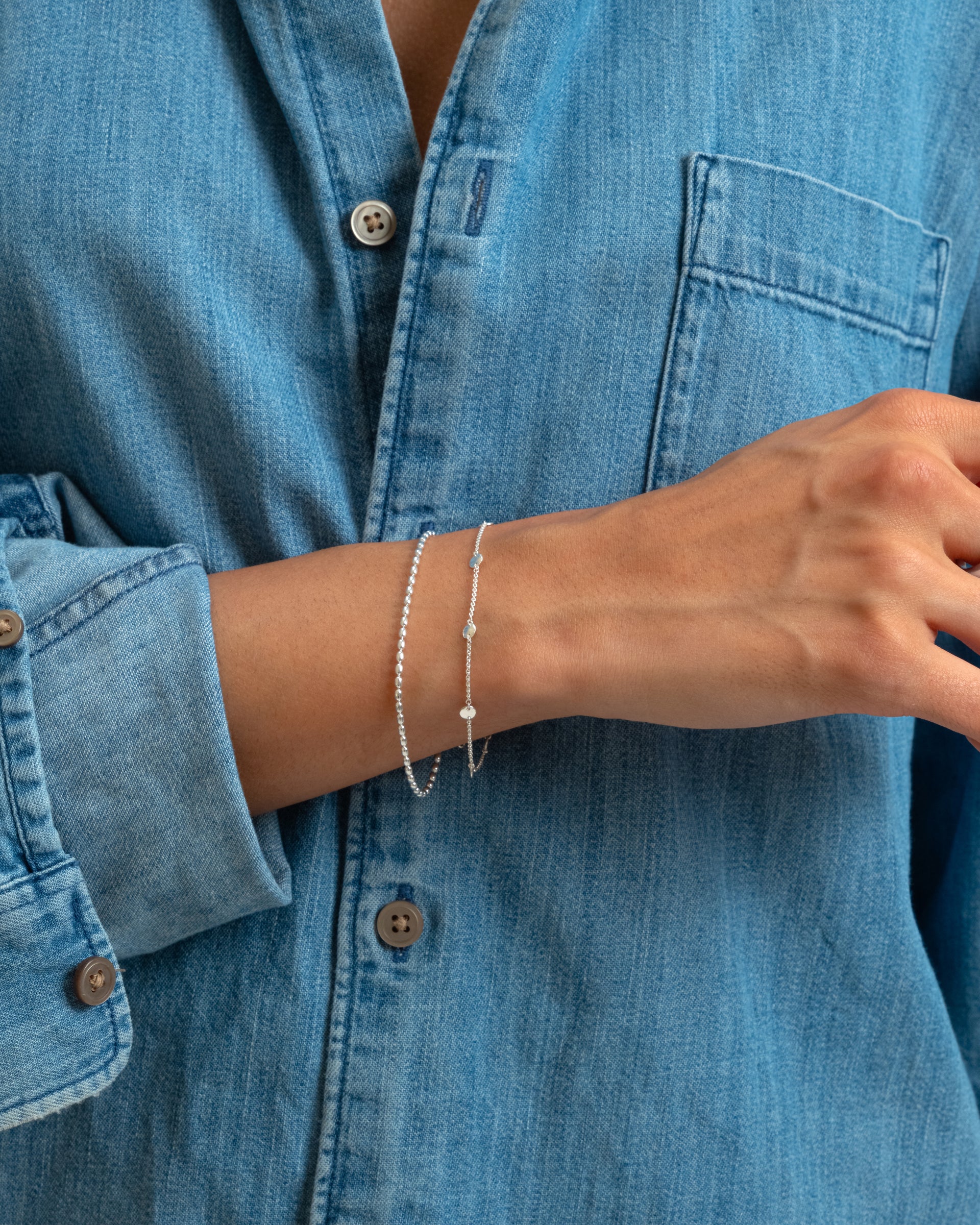 A close-up of a model wearing the silver Lunetta Bracelet, which has a ball chain design with oval beads, stacked with another delicate silver bracelet.