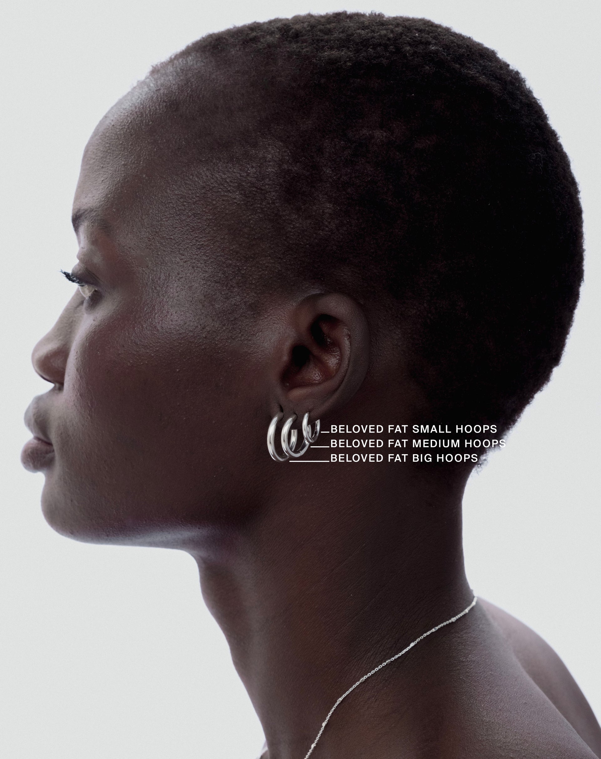 A side profile shot of a model wearing the Beloved Fat Hoops Set in silver, which includes three chunky hoops in graduating sizes stacked on her earlobe. A delicate silver chain necklace is also visible.