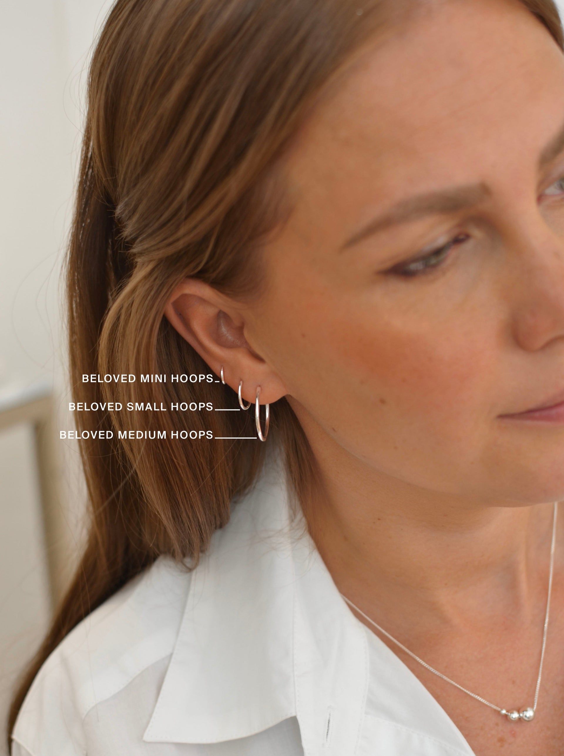 A model's ear showing the size comparison of three silver hoop earrings: the Beloved Mini Hoops, the Beloved Small Hoops, and the Beloved Medium Hoops.