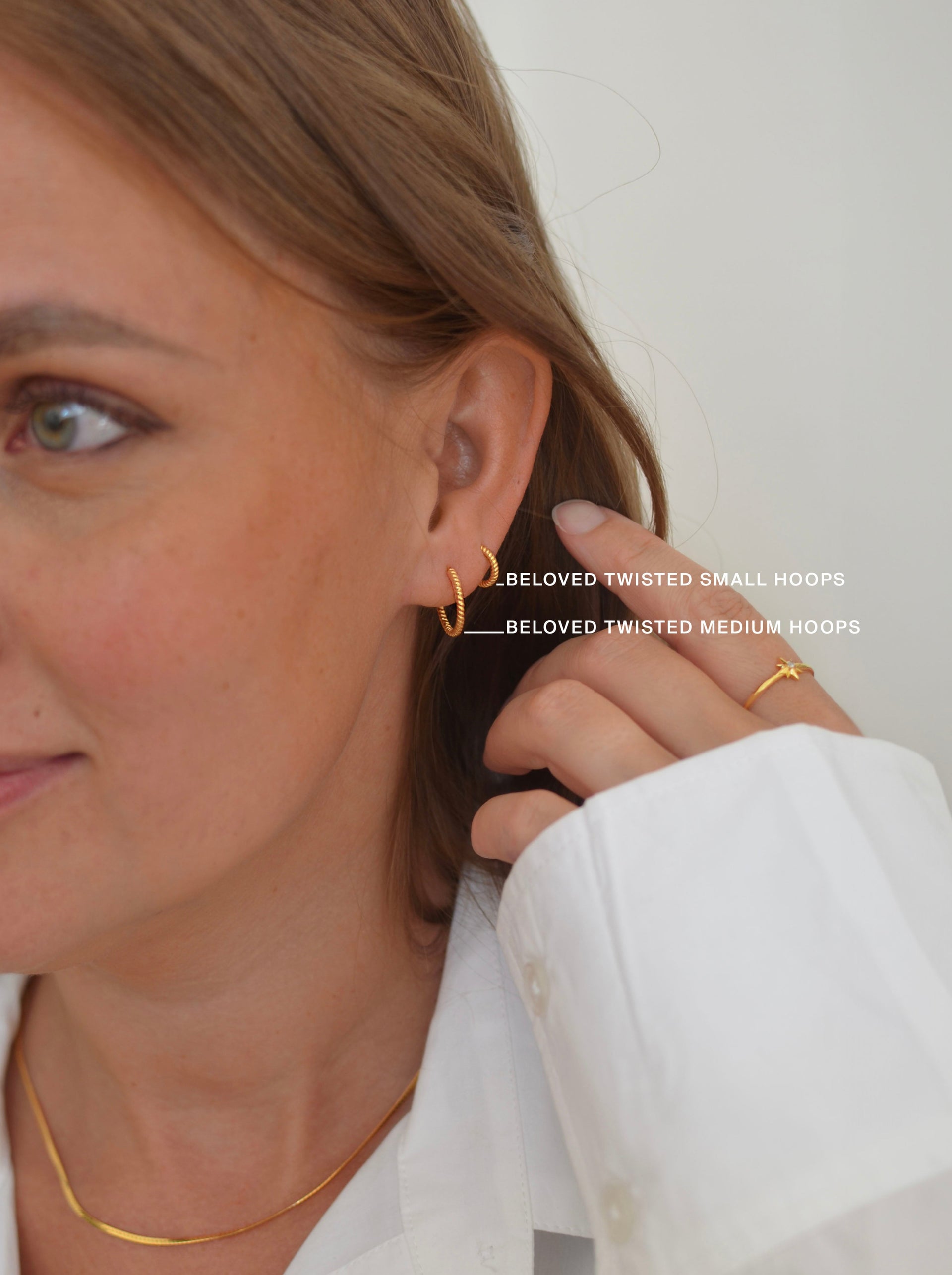 A close-up of a model wearing the Beloved Twisted Medium and Small Hoops in gold, paired with a delicate gold ring and a gold snake chain necklace.