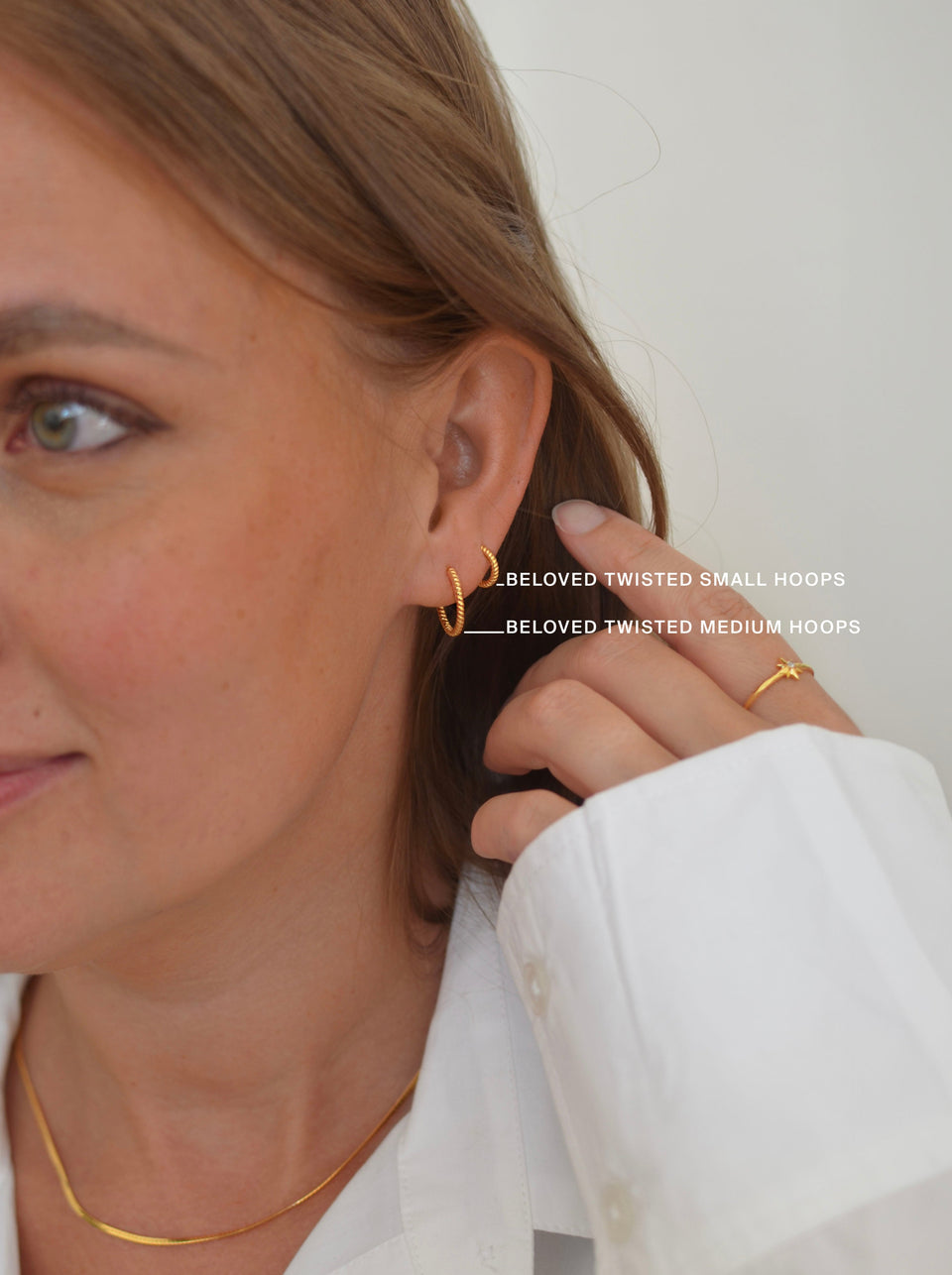 A close-up shot of a model wearing both the Beloved Twisted Small Hoops and the Beloved Twisted Medium Hoops in gold, along with a gold chain necklace and a star-shaped ring.