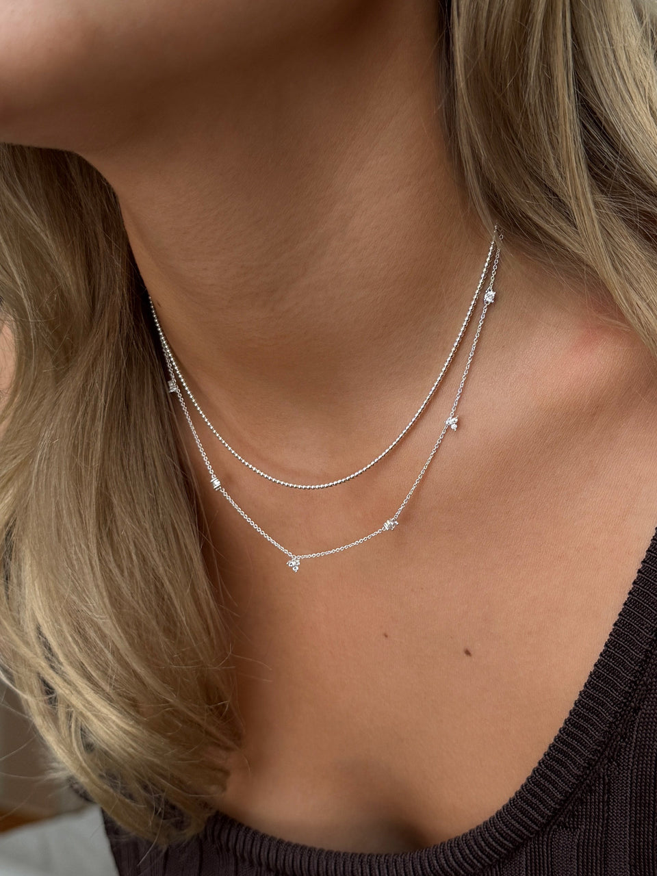 Two layered silver necklaces: a beaded chain paired with a delicate chain featuring small cubic zirconia stones.