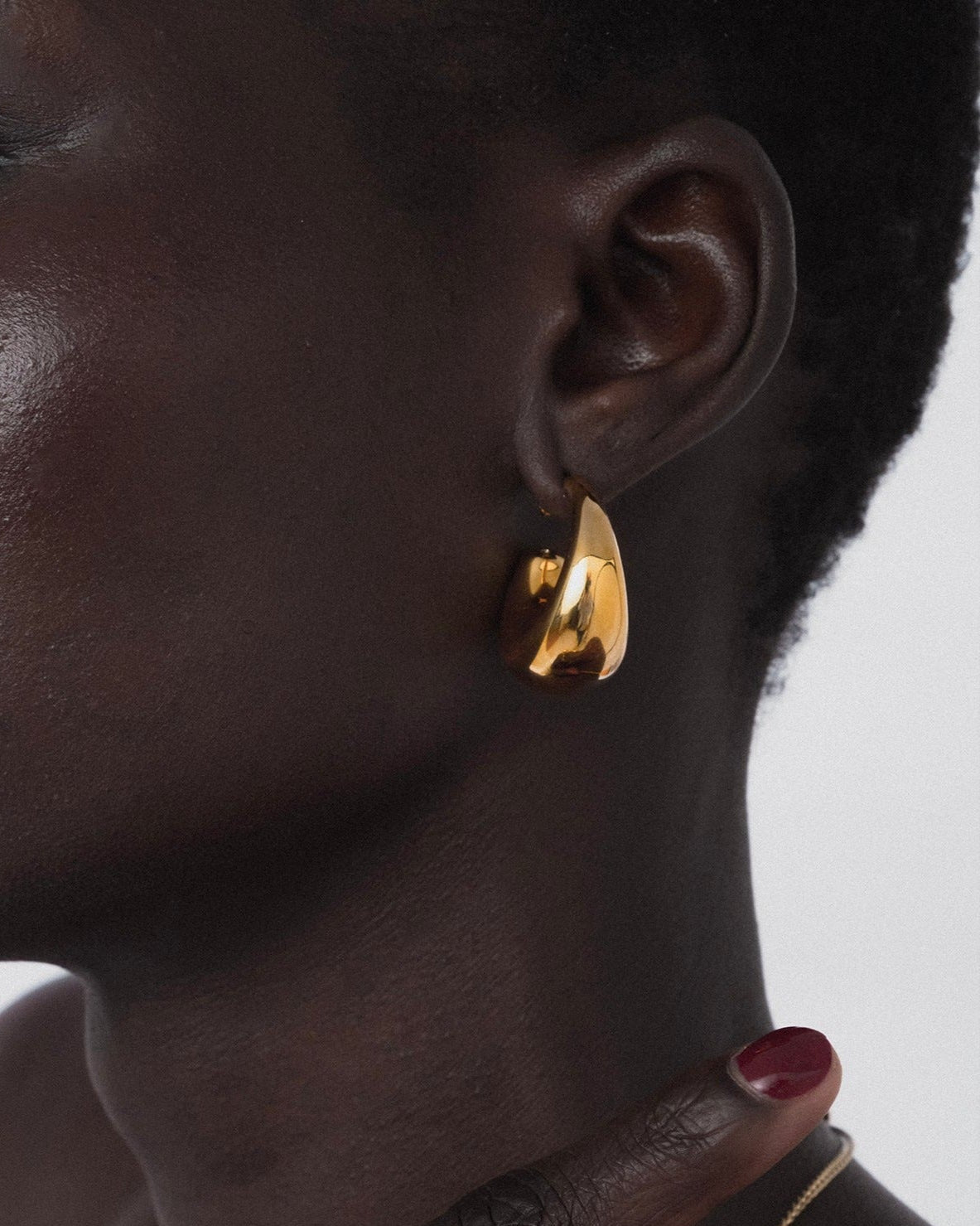 A close-up shot of a model wearing the Bolded Earrings in gold, highlighting their chunky and unique hoop shape.