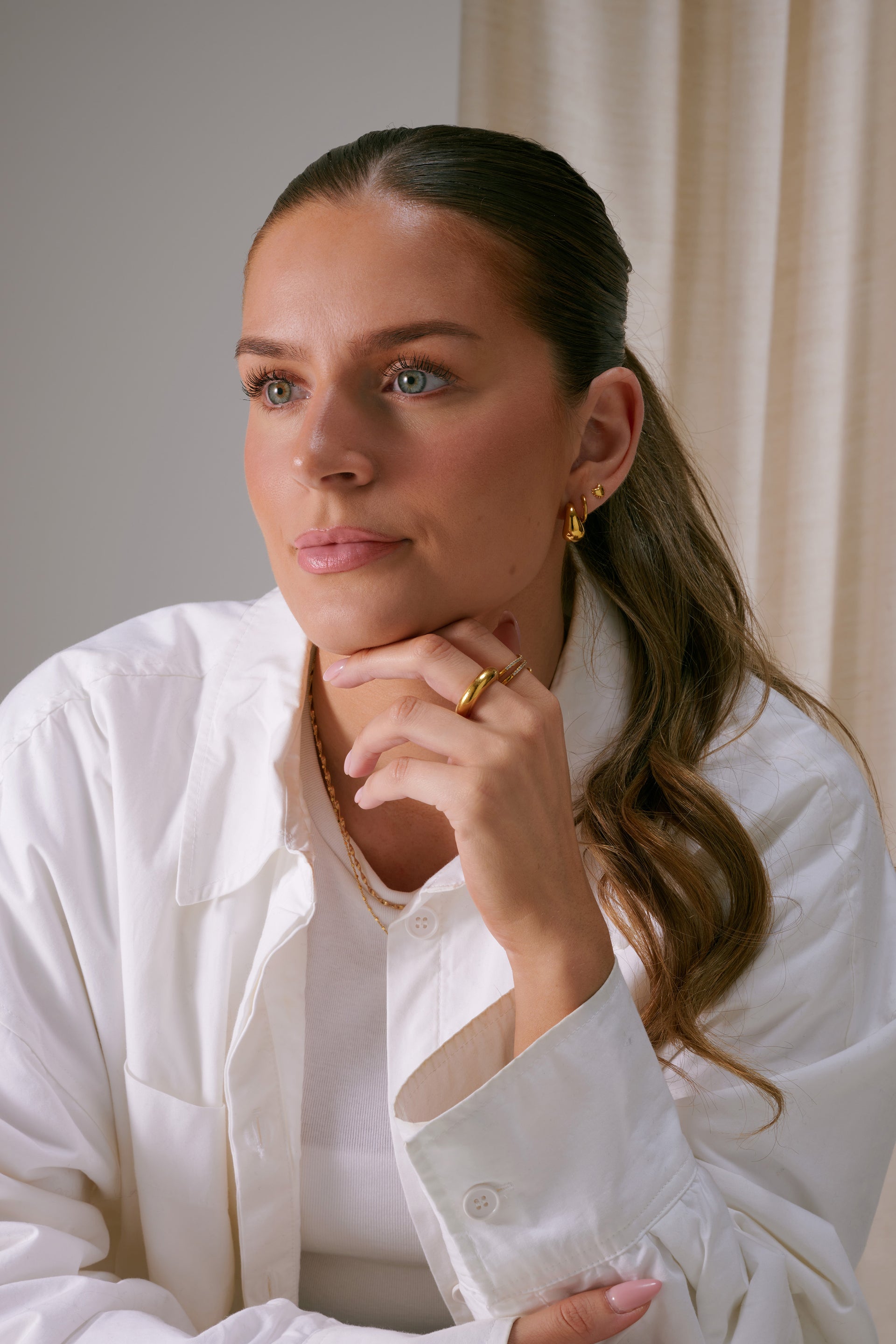 Gold small hoop earrings styled with several smaller gold earrings, a layered gold chain necklace, and a thick gold ring.