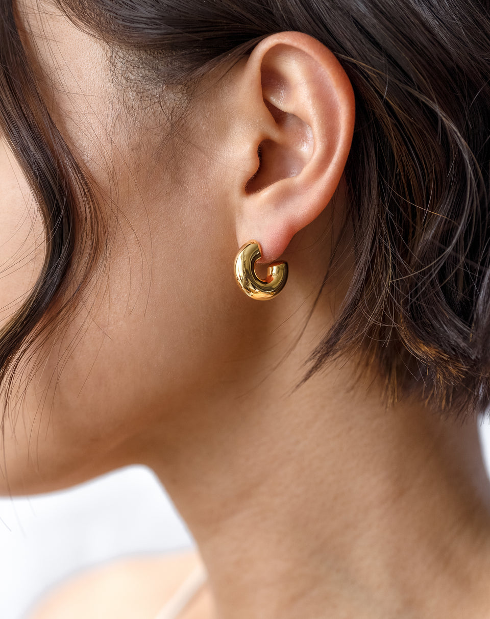 A close-up shot of a model wearing the Bolded Little Sis Hoops in gold, showcasing the small, chunky design.