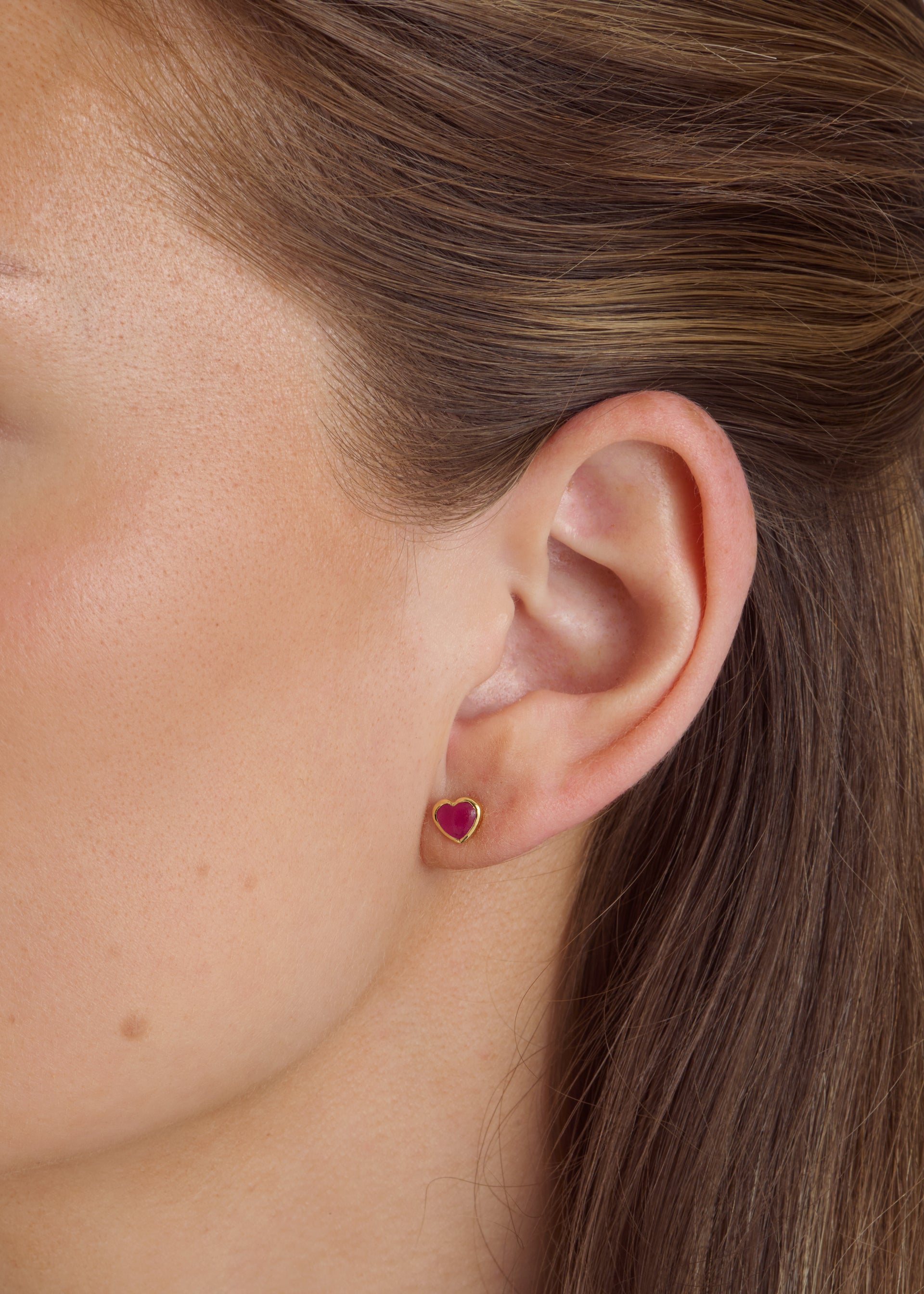Close-up of a model wearing the La La Love stud earring, a delicate gold heart set with a vibrant pink quartz stone.