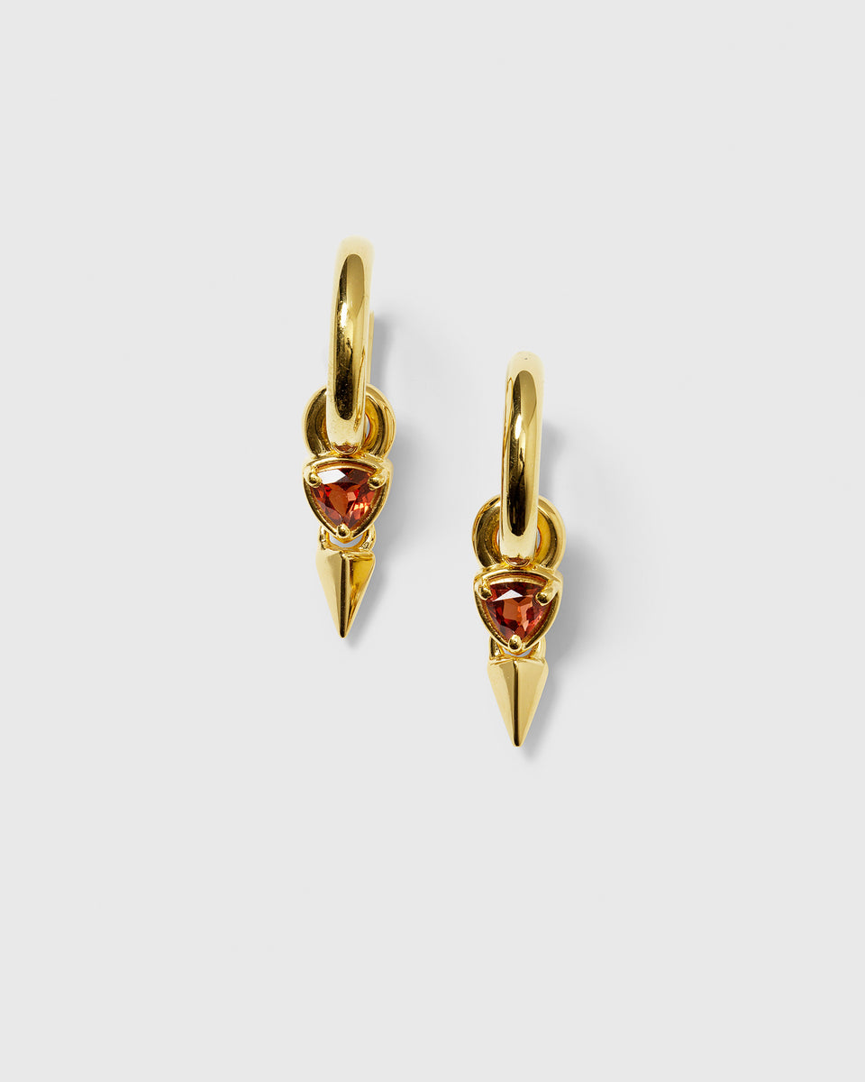 A product shot of the Mrs H Spike Earrings in gold, featuring a chunky hoop with a dangling charm composed of a triangular garnet and a pointed spike.