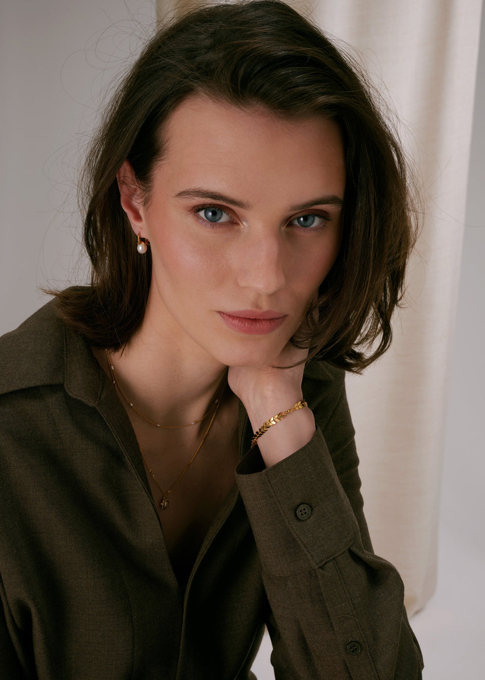 Gold pearl earrings, leaf-design gold bracelet, and layered fine gold necklaces.