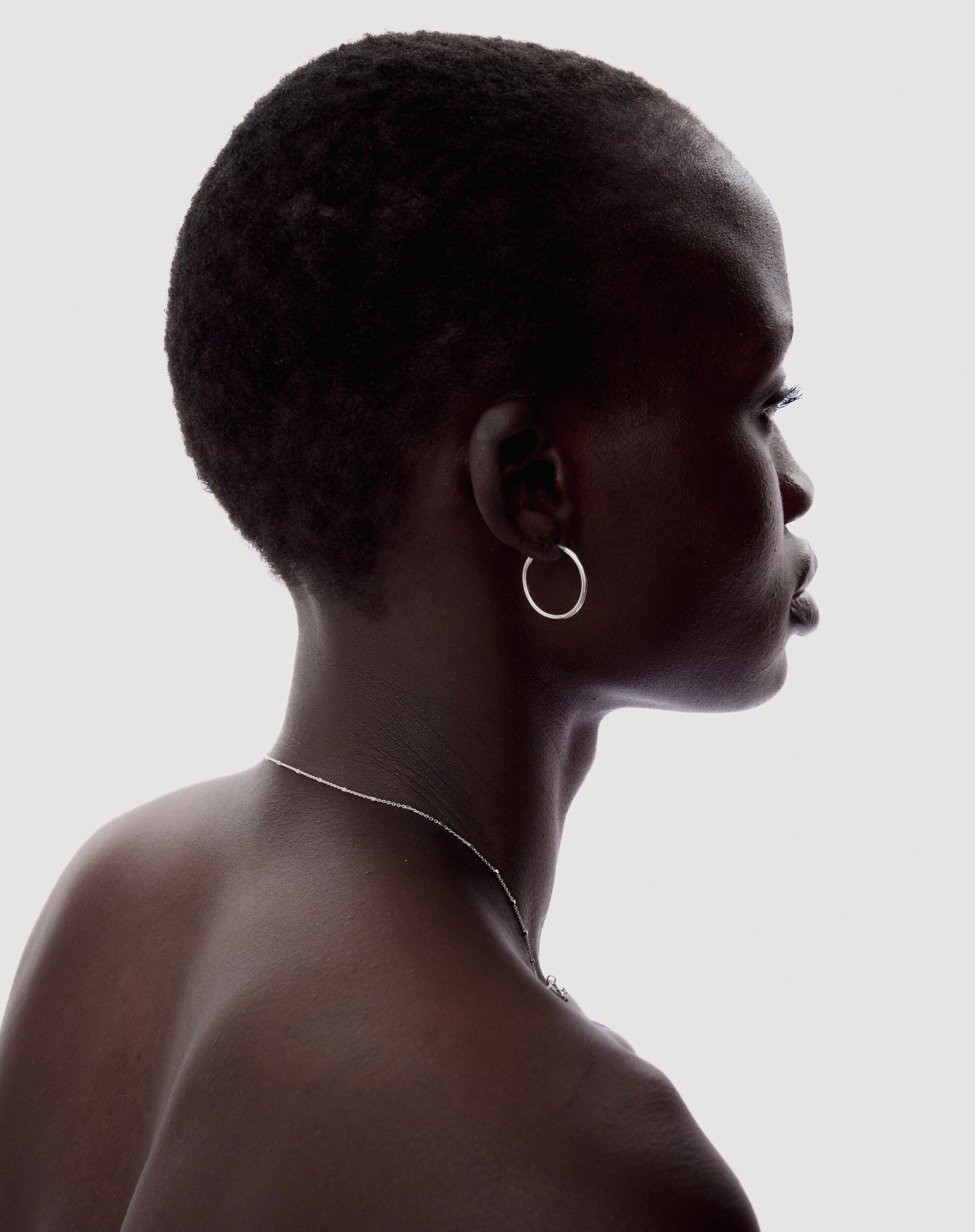 A close-up profile of a model wearing the Beloved Medium Hoops in silver and a thin silver chain necklace.
