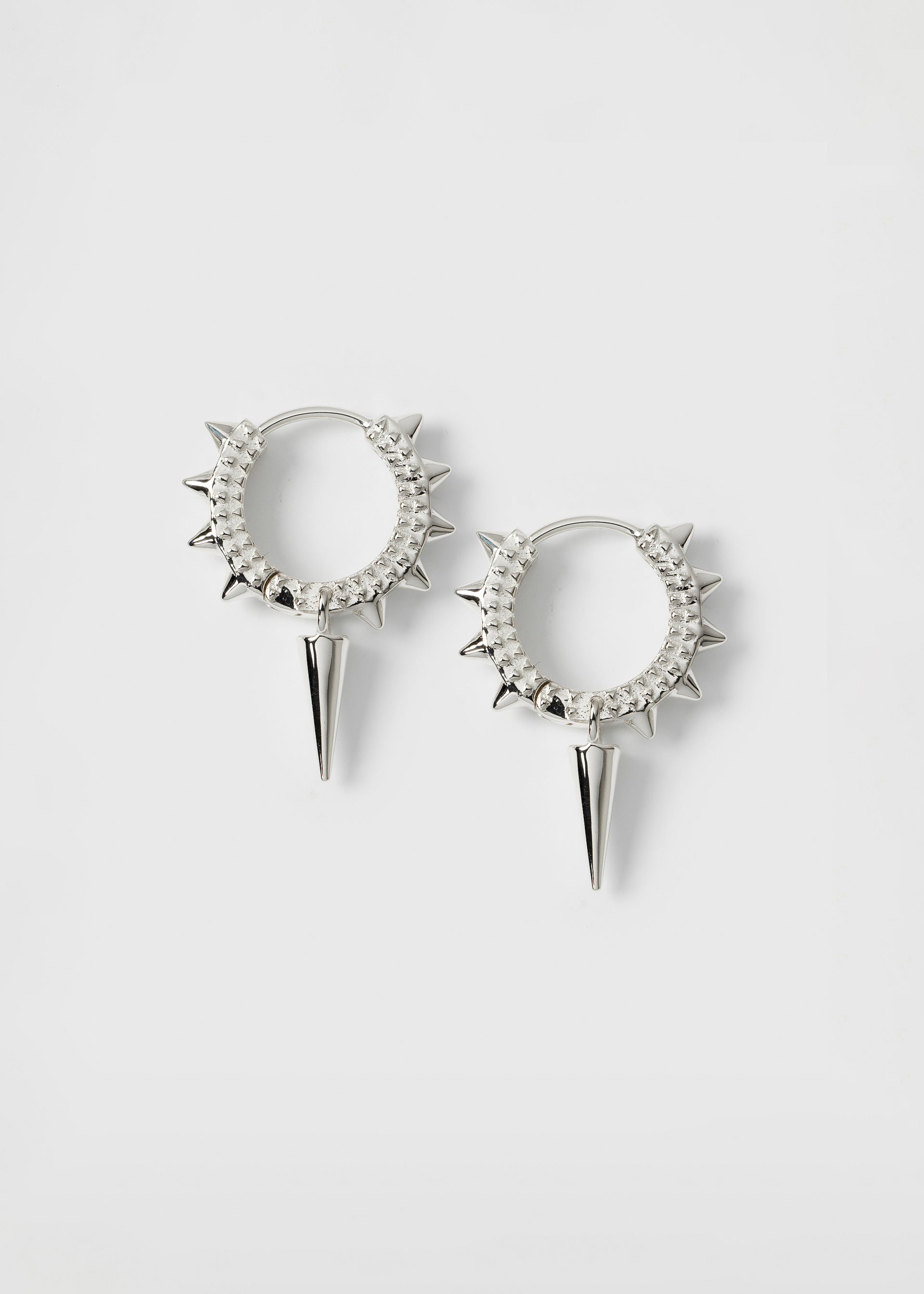 A product shot of the silver Harvey Heavy Spike Hoops, featuring a pair of textured hoops with small spikes along the outer edge and a larger, dangling spike charm on each earring.