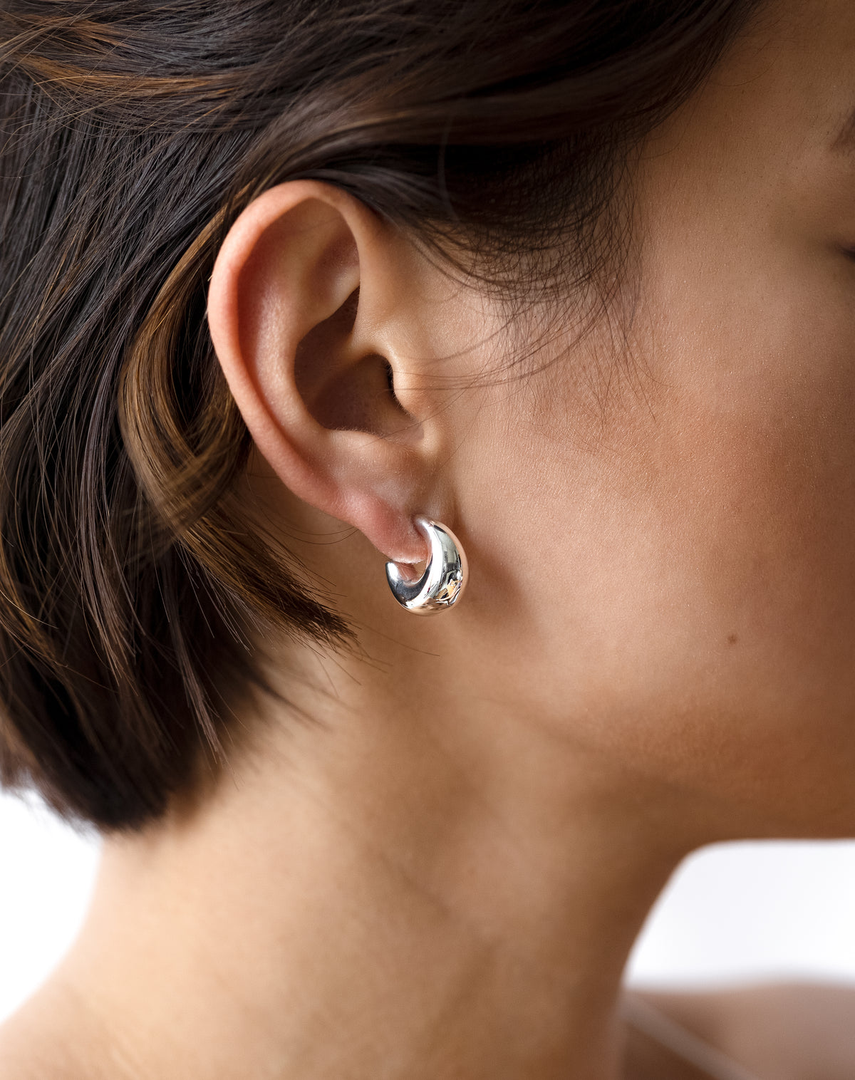 A close-up of a model wearing the Bolded Little Sis Earrings in silver, highlighting their chunky, rounded design.