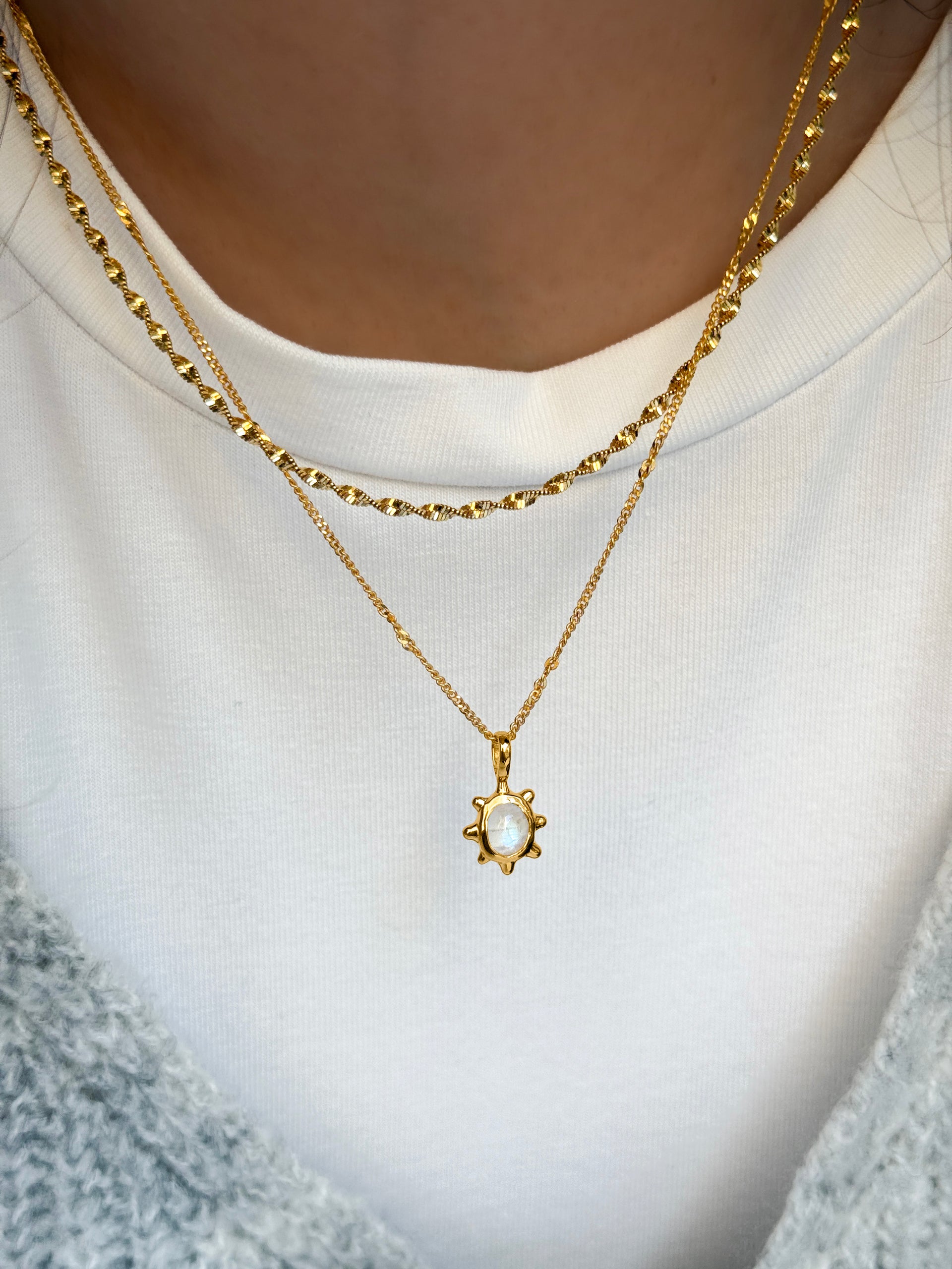 A close-up shot of a model wearing the Florentina Necklace in gold, featuring a flower-shaped pendant with a moonstone, layered with a shorter twisted gold chain necklace.