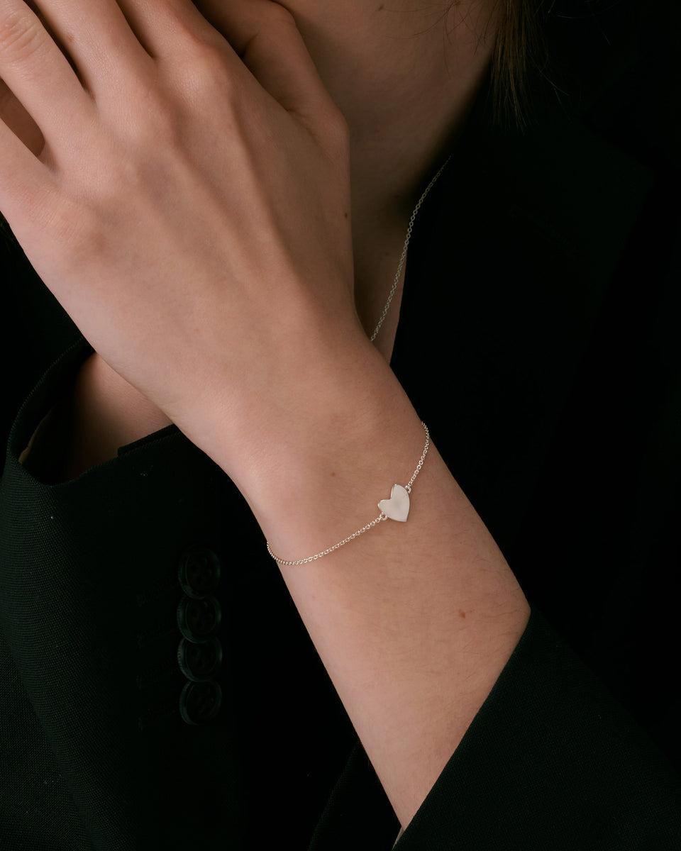 A delicate silver chain bracelet with a hammered heart charm, paired with a fine silver chain necklace.