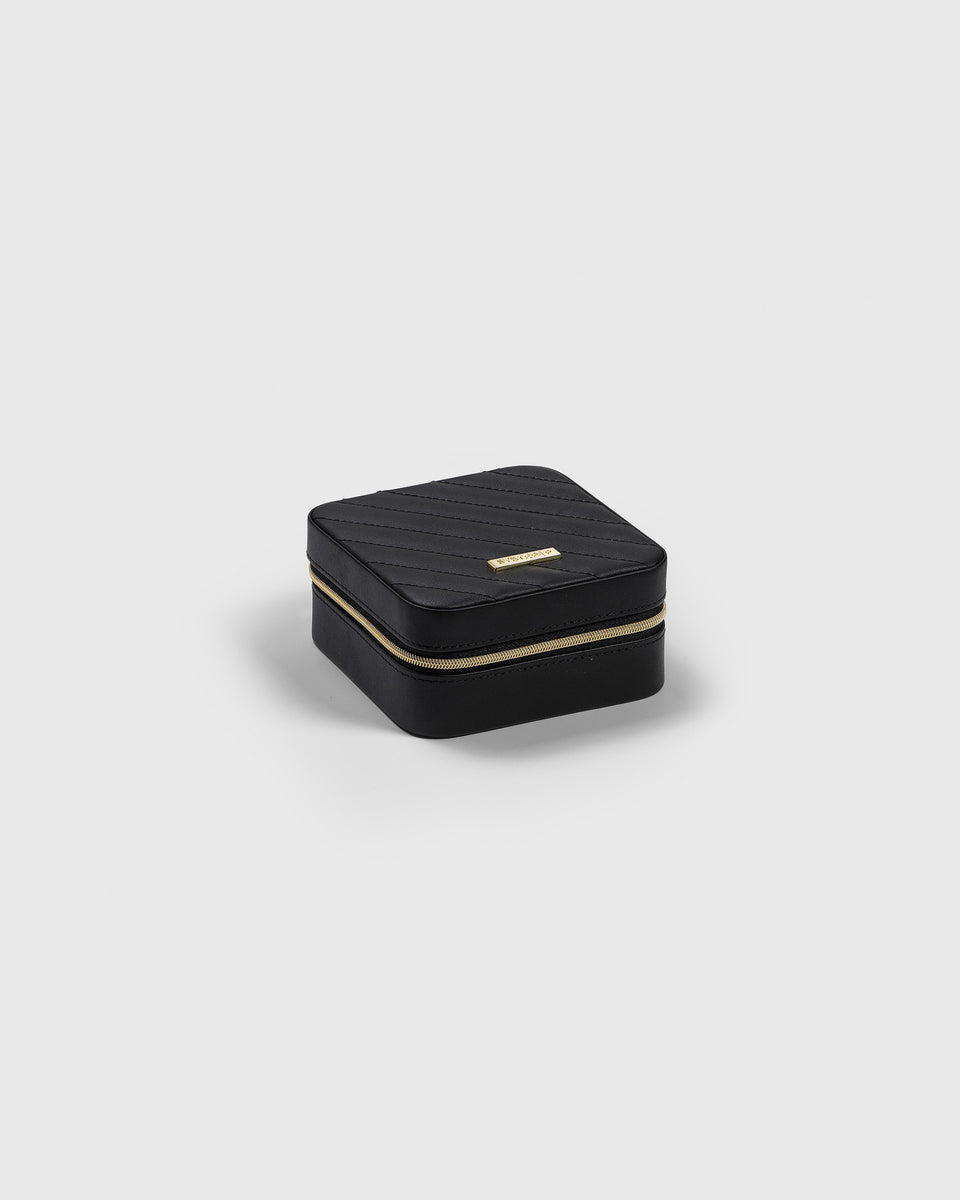 A product shot of the small, black Syster P jewelry case, showing its quilted top, gold zipper, and brand plaque.