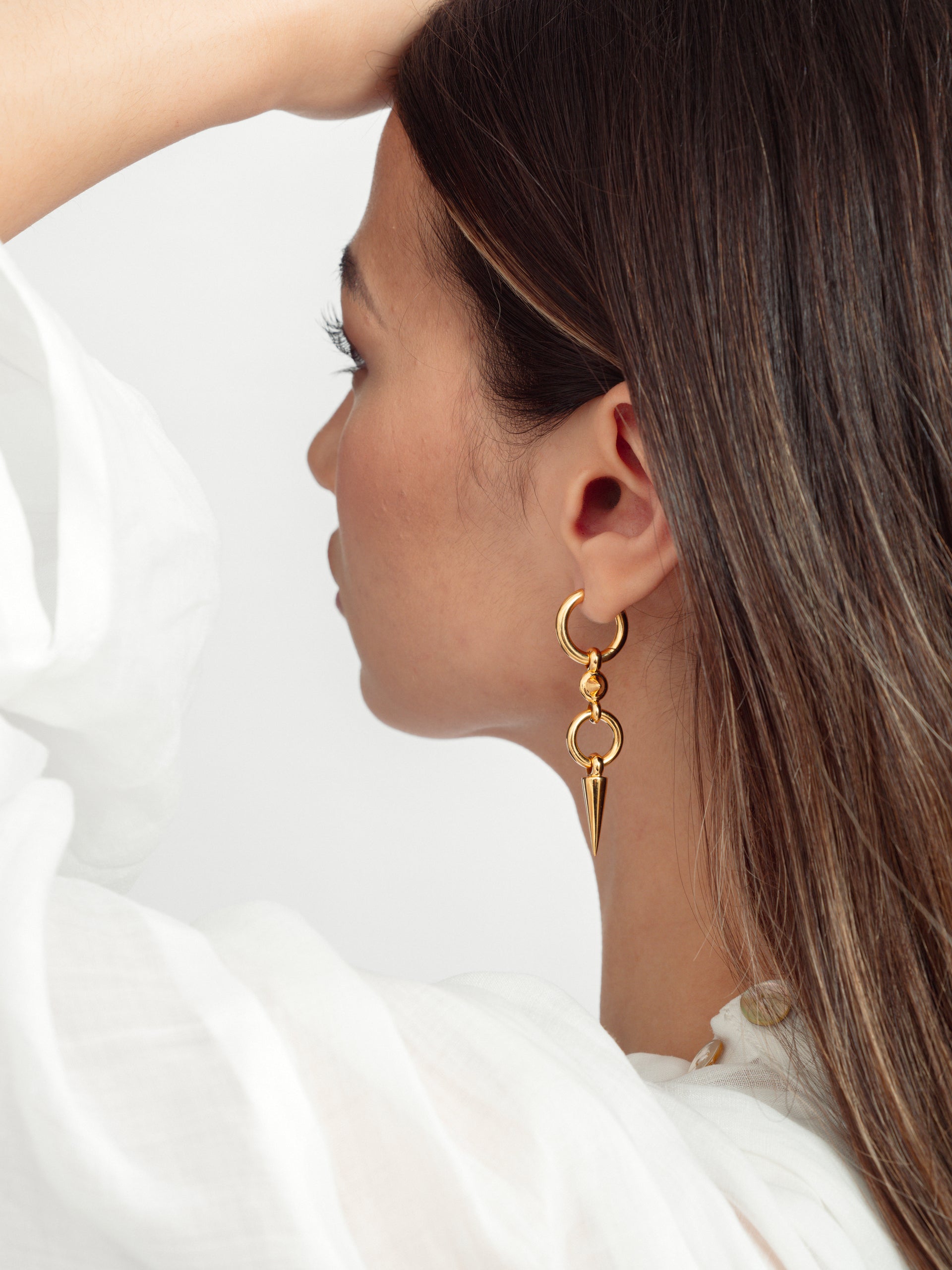 A close-up shot of a model wearing the Juno Long Single Earring in gold, featuring a chunky hoop with a long, dangling spike.