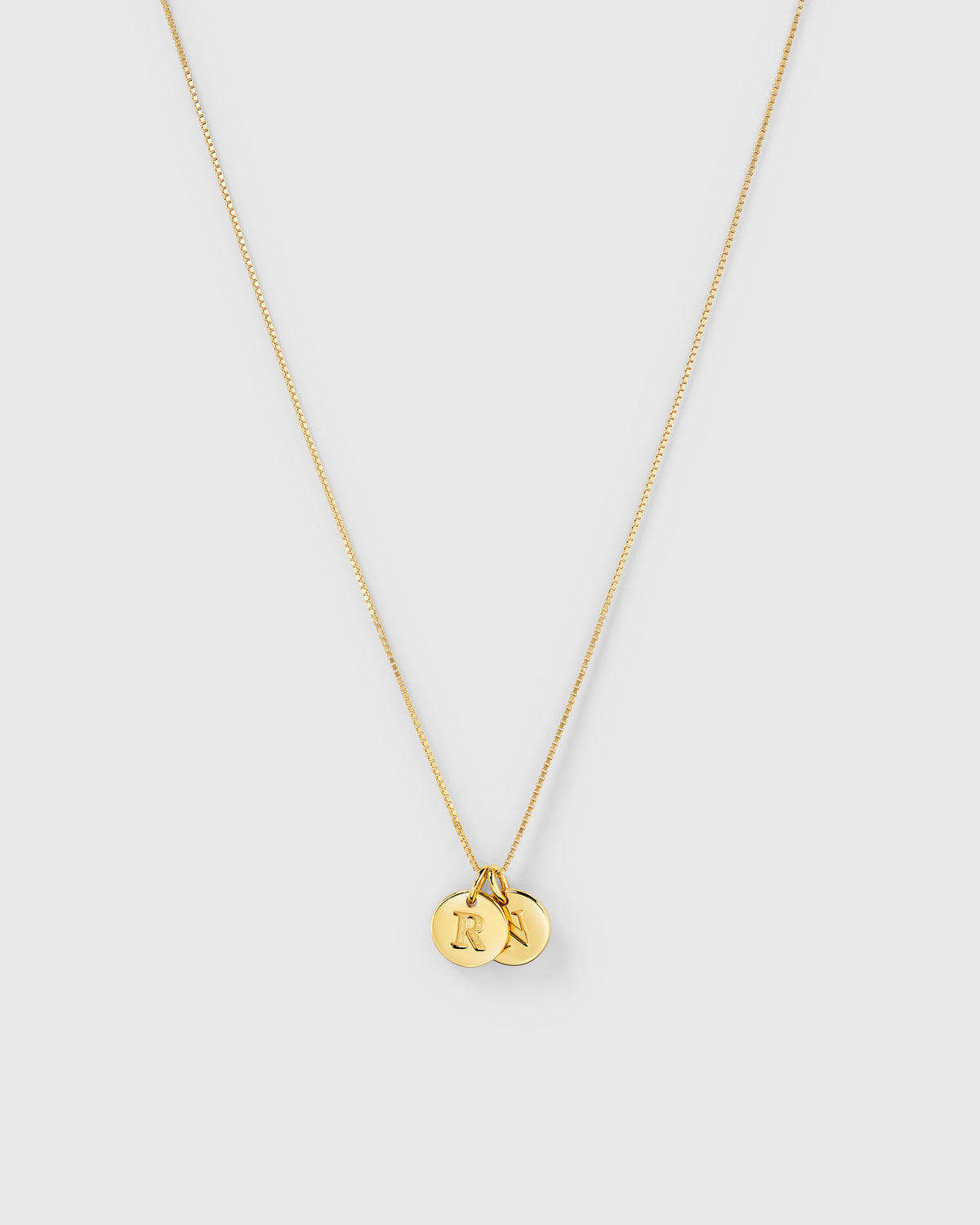 A product shot of the Beloved Medium Box Chain in gold, styled with two Beloved Mini Letter charms featuring the initials 'R' and 'N'.