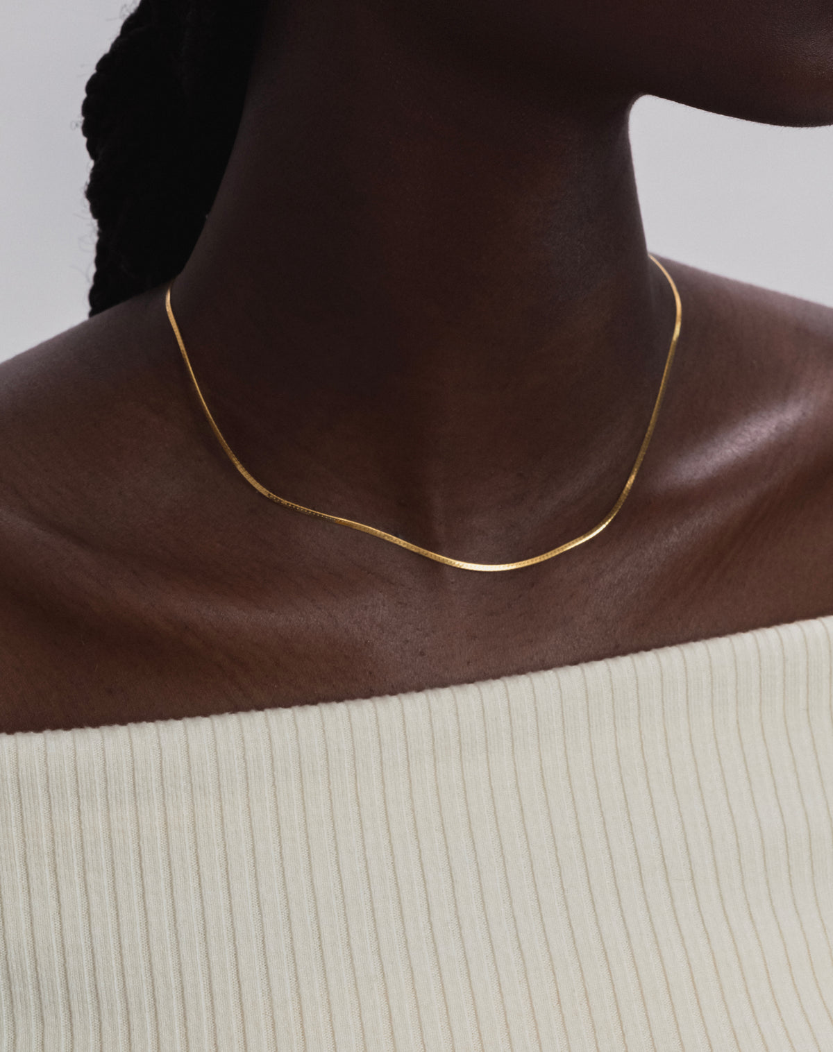 A close-up shot of a model wearing the Herringbone Necklace in gold, showcasing its smooth and delicate flat chain design.