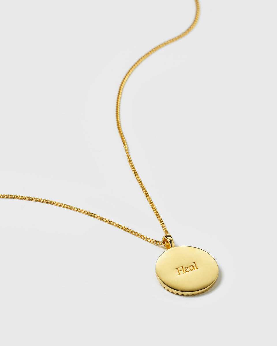 A product shot of the Lucky Coin Heal Necklace in gold, displaying the back of the round coin pendant which has the word 'Heal' engraved on it.