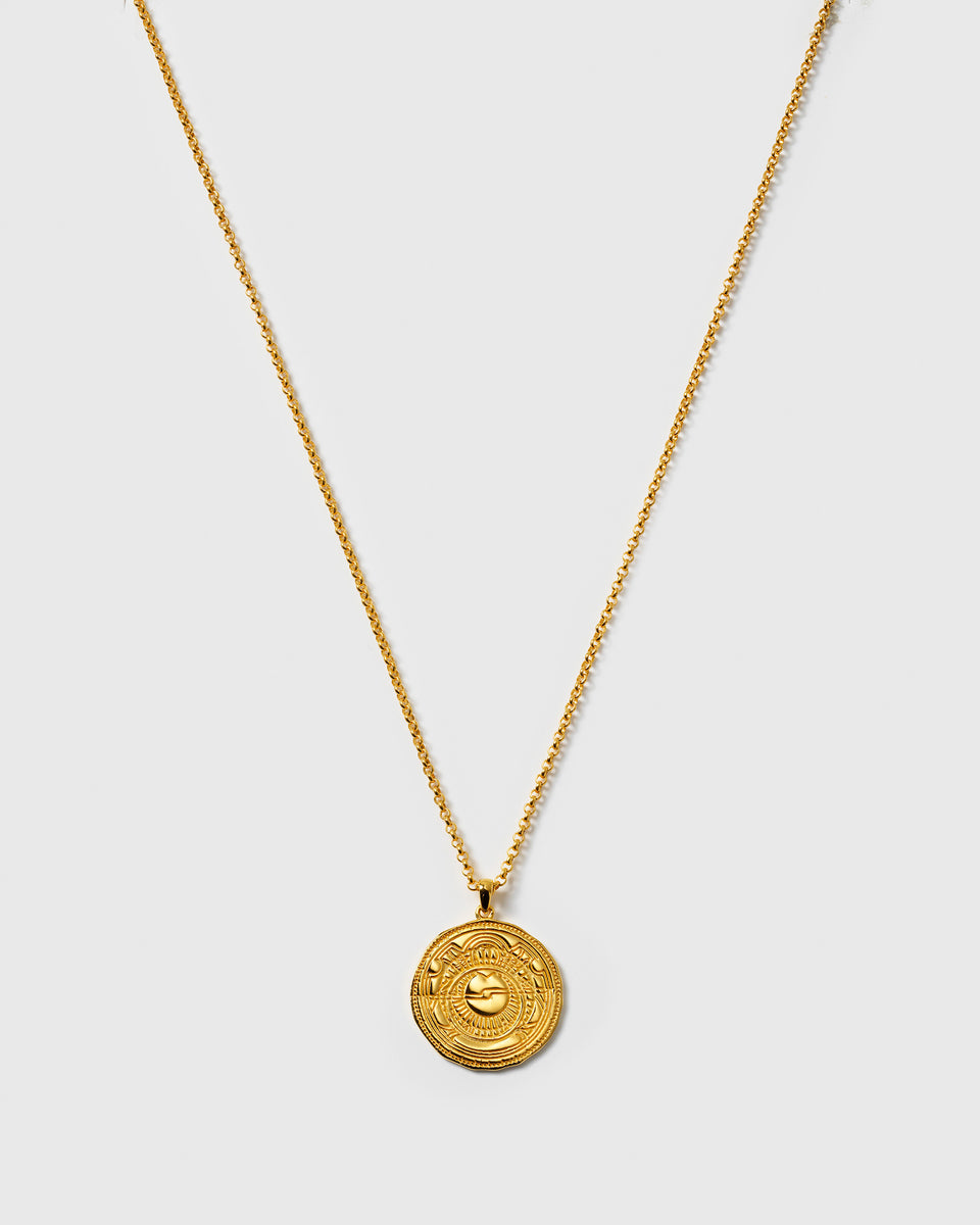 A product shot of the Lucky Coin Navigate Necklace in gold, featuring a fine chain and a round, coin-like pendant with an embossed compass design.