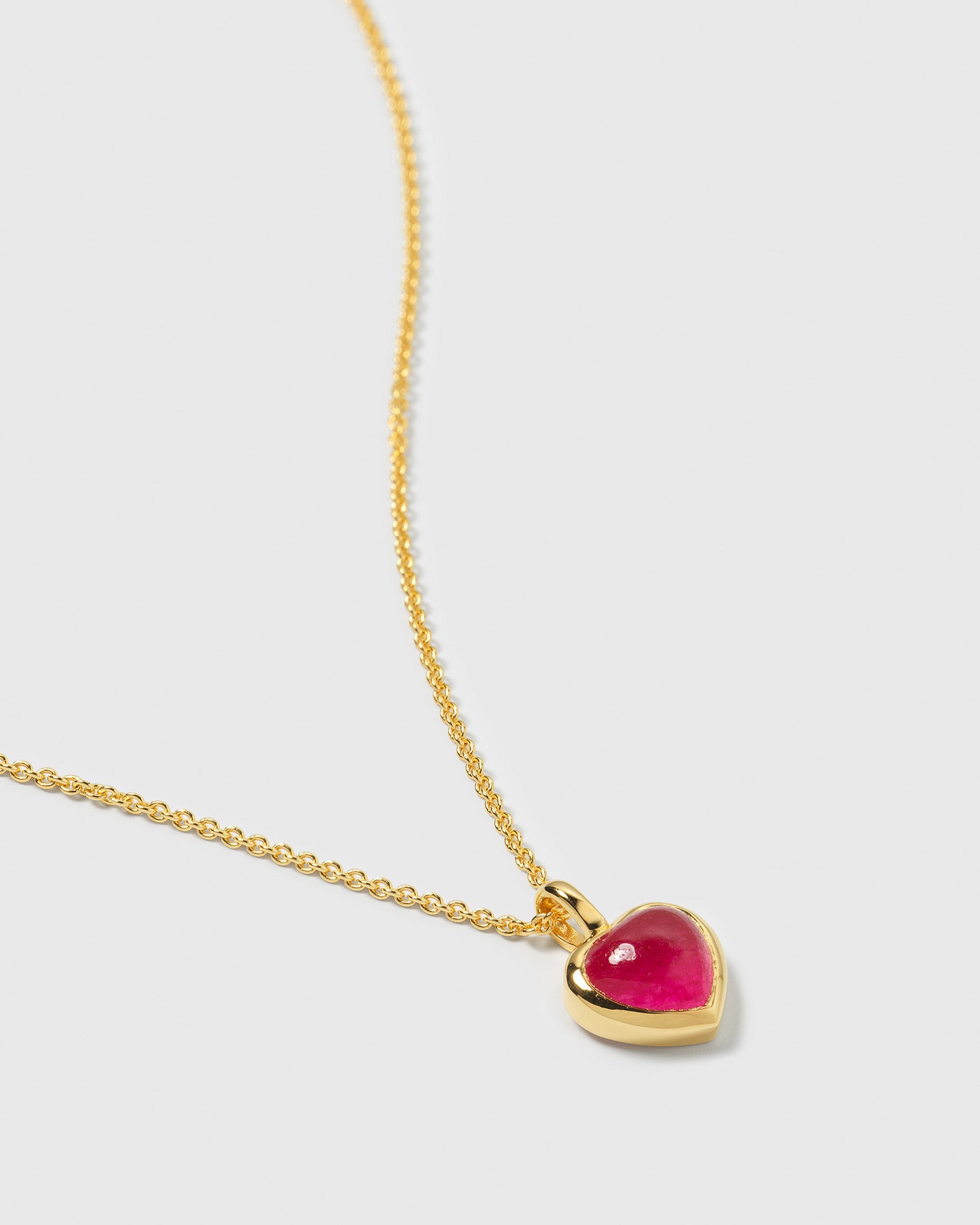 A close-up photo of the La La Love gold necklace, featuring a delicate chain and a heart-shaped pendant with a pink quartz stone.