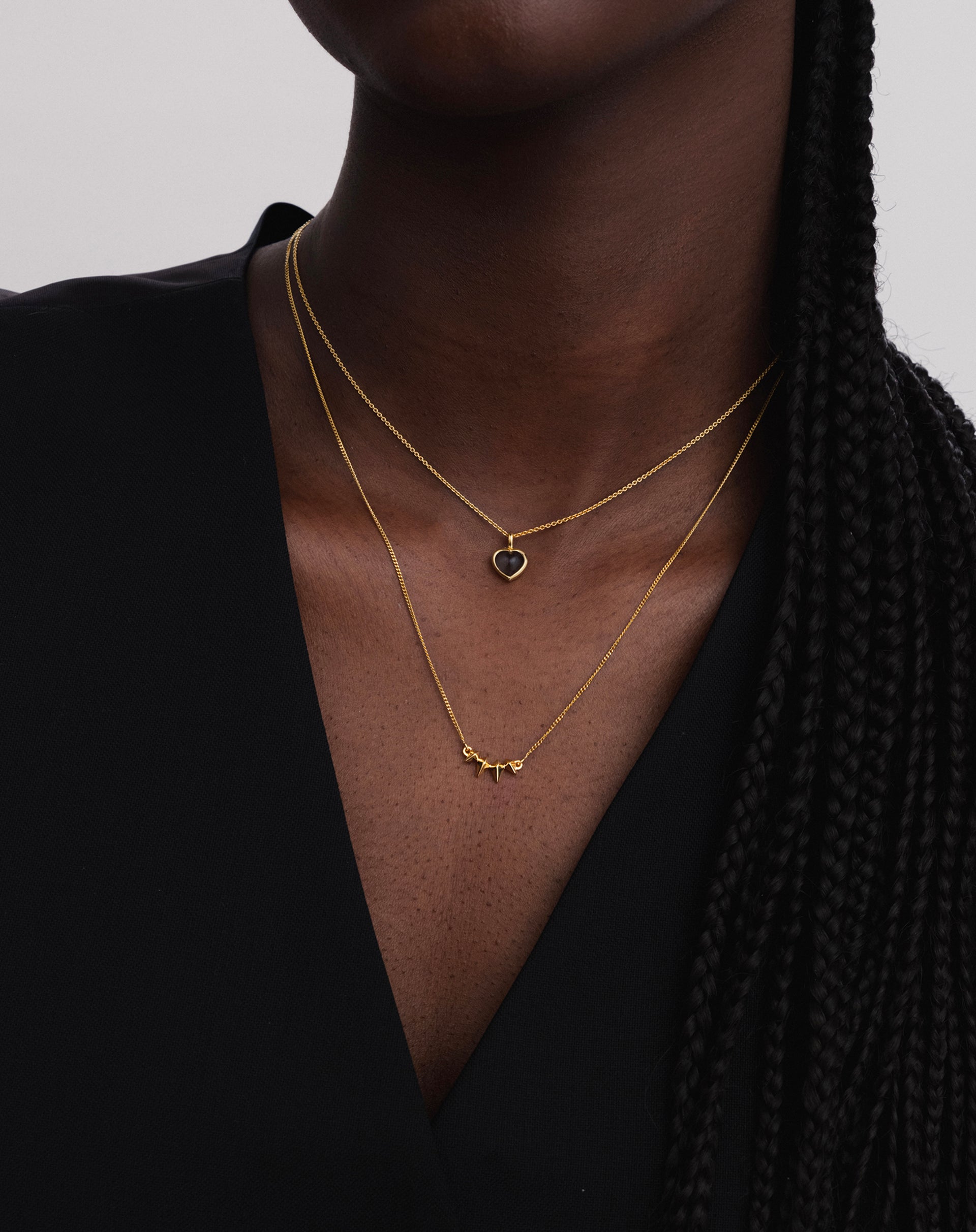 A model wears the gold Uma Spike Necklace, layered with a shorter gold chain necklace that has a small black heart pendant.