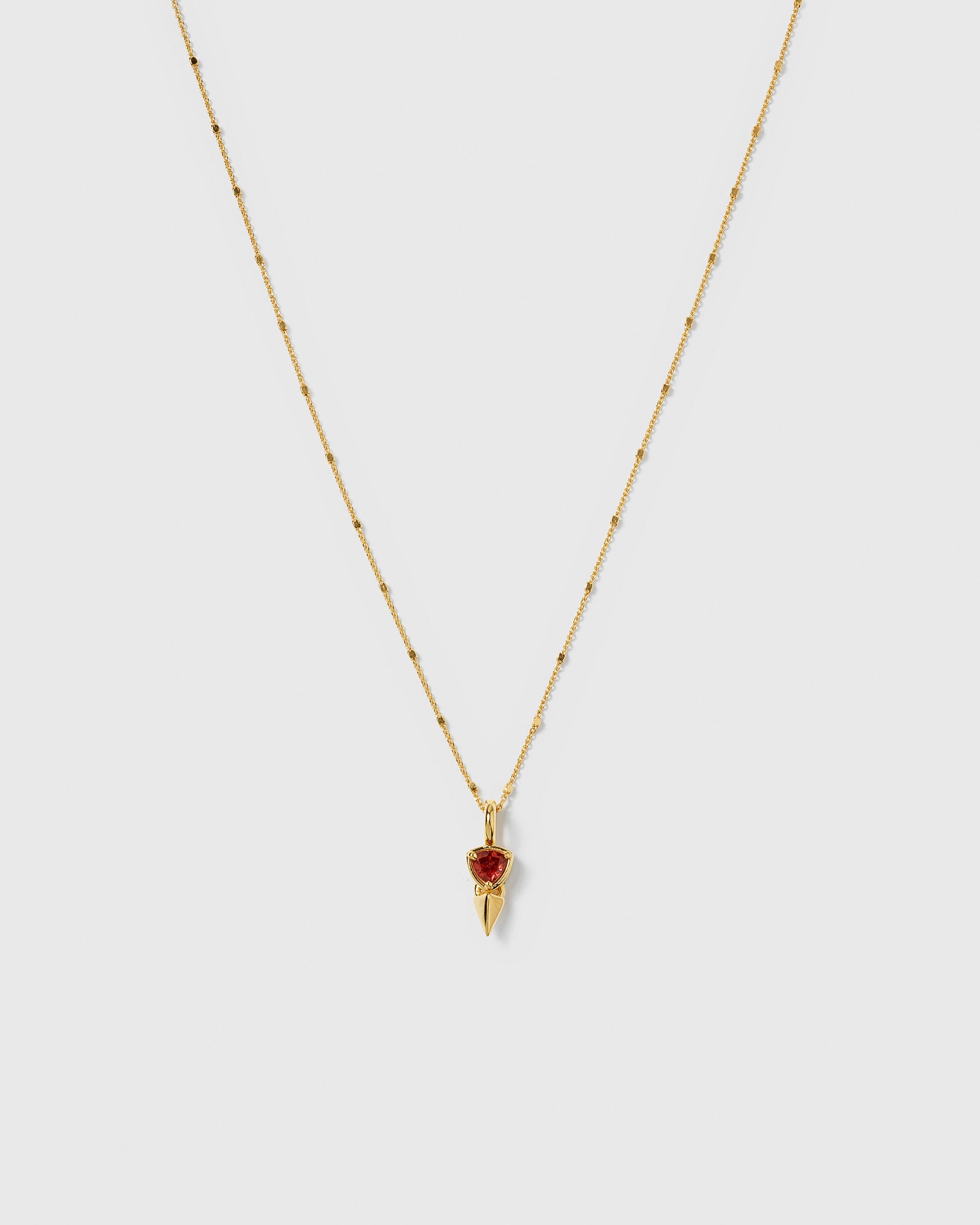 A product shot of the Mrs H Spike Necklace in gold, highlighting its delicate beaded chain and pendant which combines a red garnet stone with a golden spike.