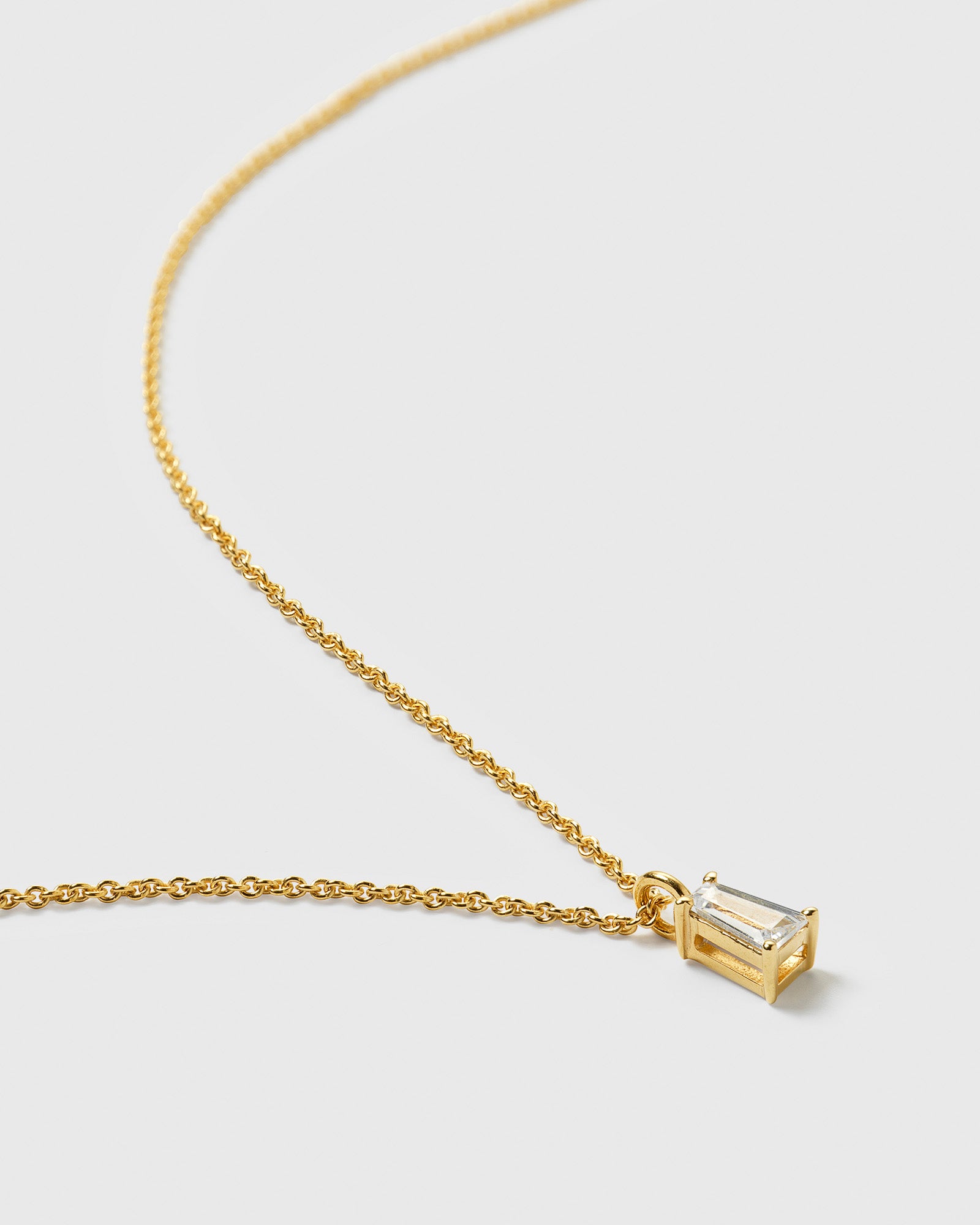 A close-up product shot of the Iggy Necklace in gold, showing its fine chain and a pendant with a tapered baguette-cut cubic zirconia.
