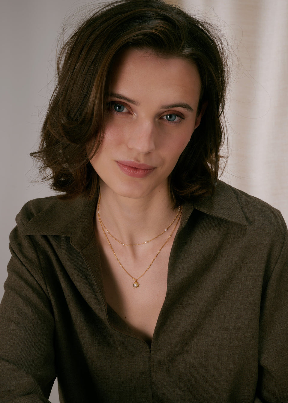 Gold layered necklaces, one with a sunburst pendant featuring a pearl, and a shorter chain decorated with freshwater pearls.