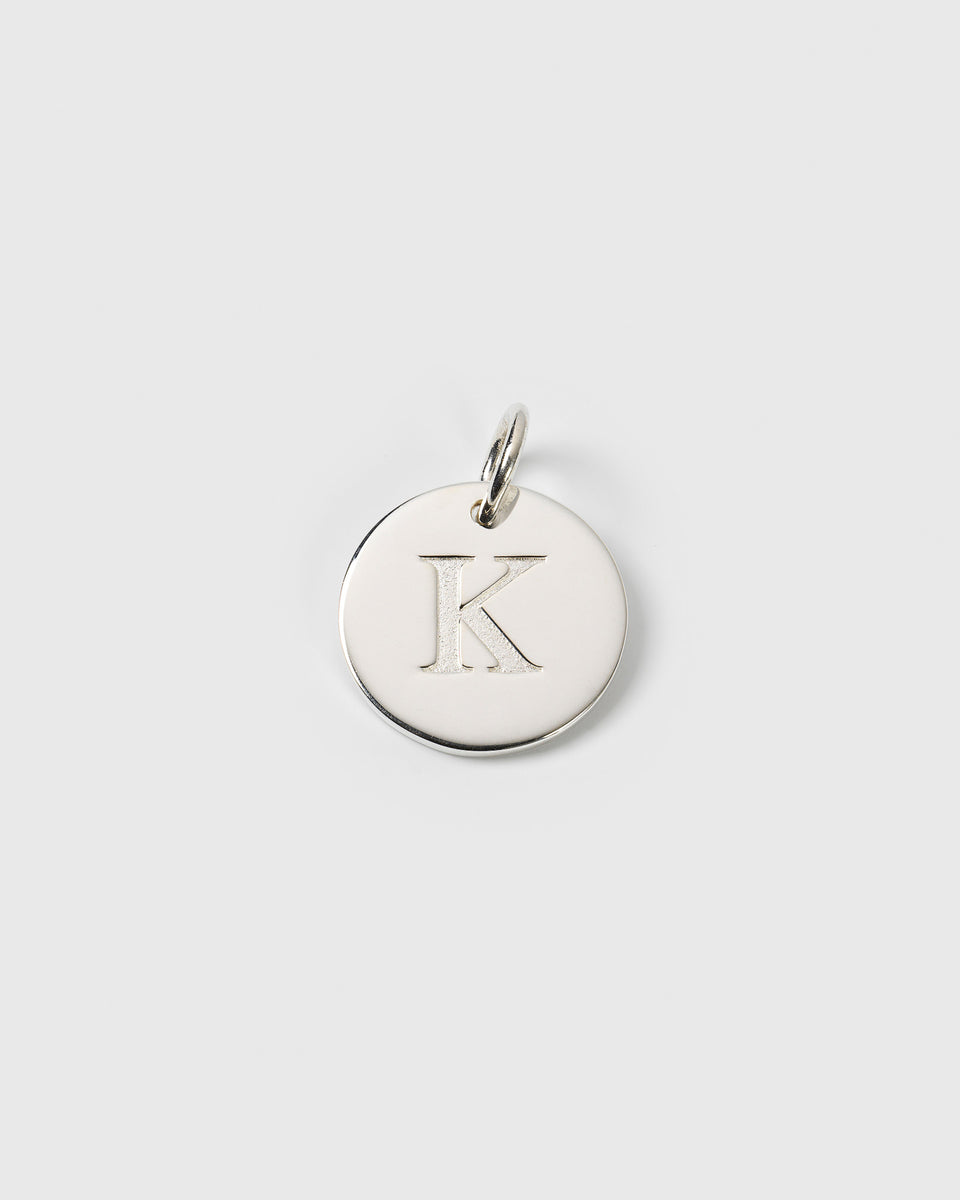 A product shot of the Beloved Big Letter Silver pendant, featuring a round silver charm with the letter 'K' engraved on its surface.