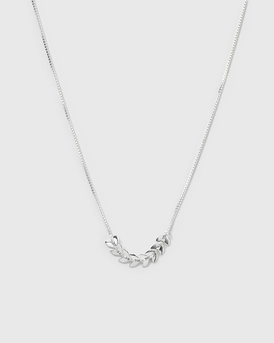 A product shot of the Layers Simone Necklace in silver, laid out to display its design of a fine chain with a central section of small, leaf-like charms.