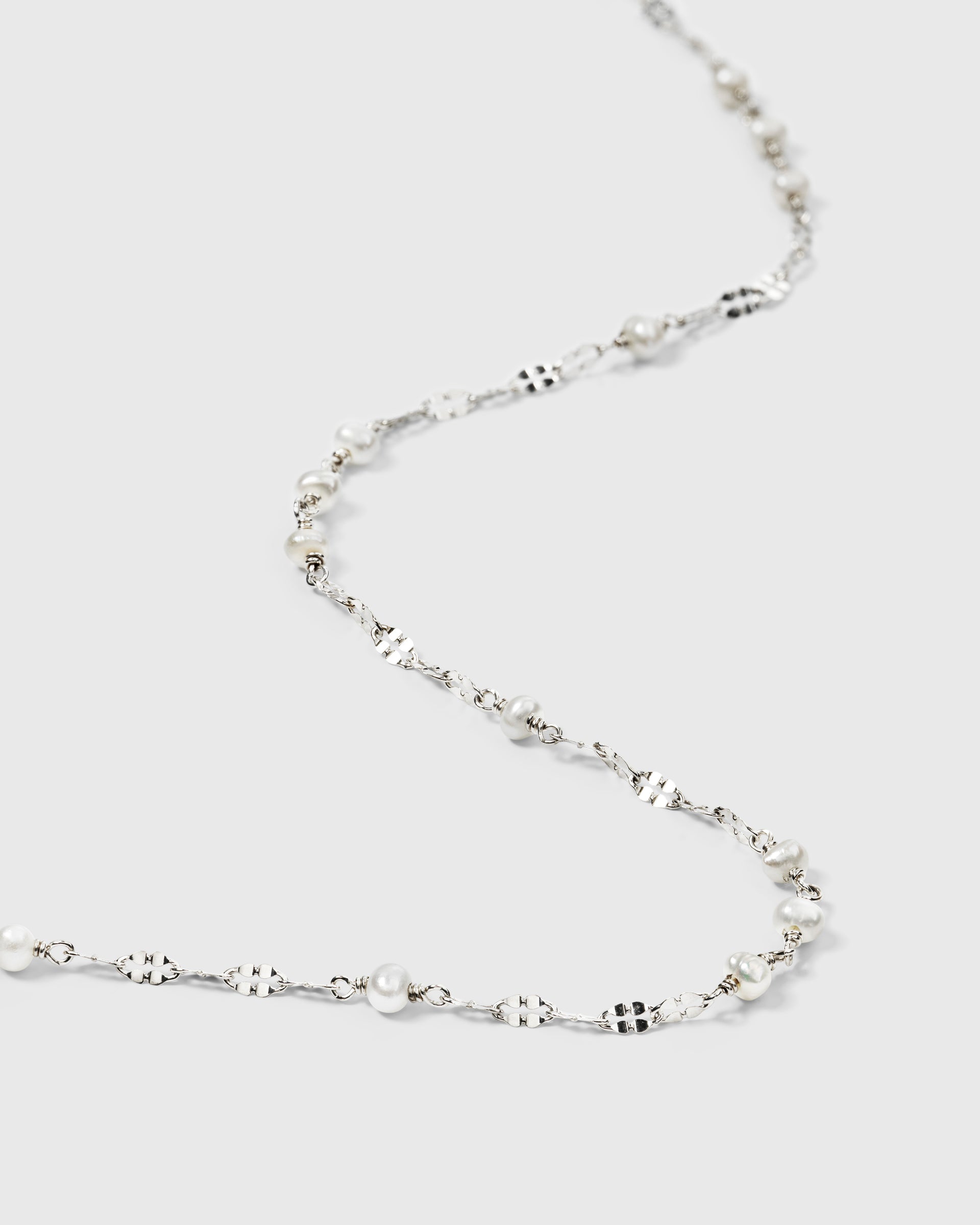 A close-up product shot of the Aurelia Necklace in silver, showcasing its unique patterned chain interspersed with small, lustrous freshwater pearls.