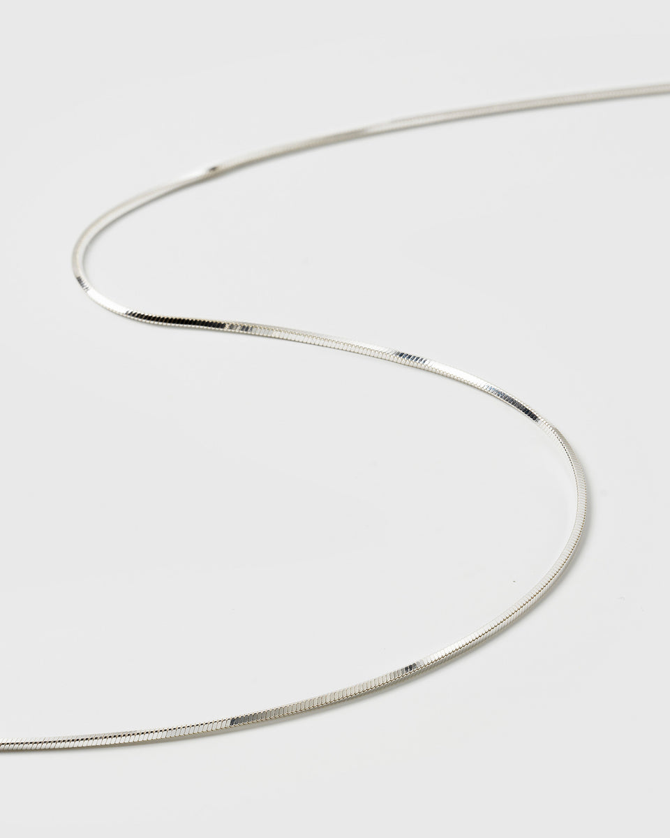 A product shot of the Sheer Mirror Necklace in silver, showing a close-up of its smooth, flat, and reflective snake chain design.