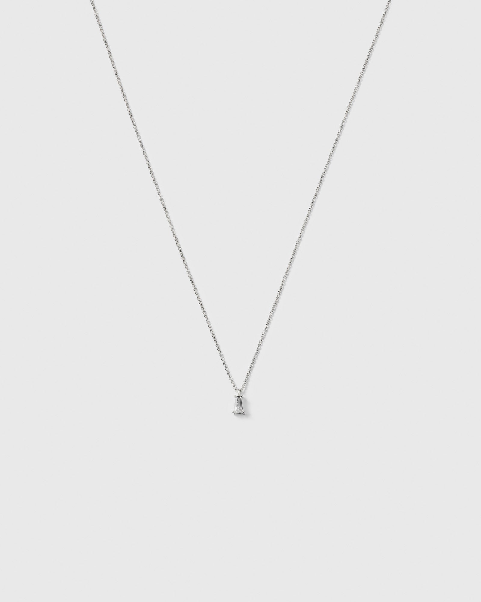 A product shot of the Iggy Necklace in silver, featuring a fine chain and a small pendant with a single, tapered baguette-cut cubic zirconia.