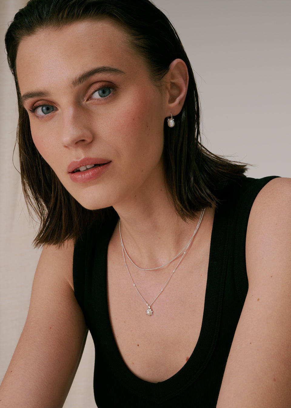 A silver necklace with a sunburst pendant featuring a freshwater pearl, layered with a silver ball chain necklace, paired with silver and pearl drop earrings.