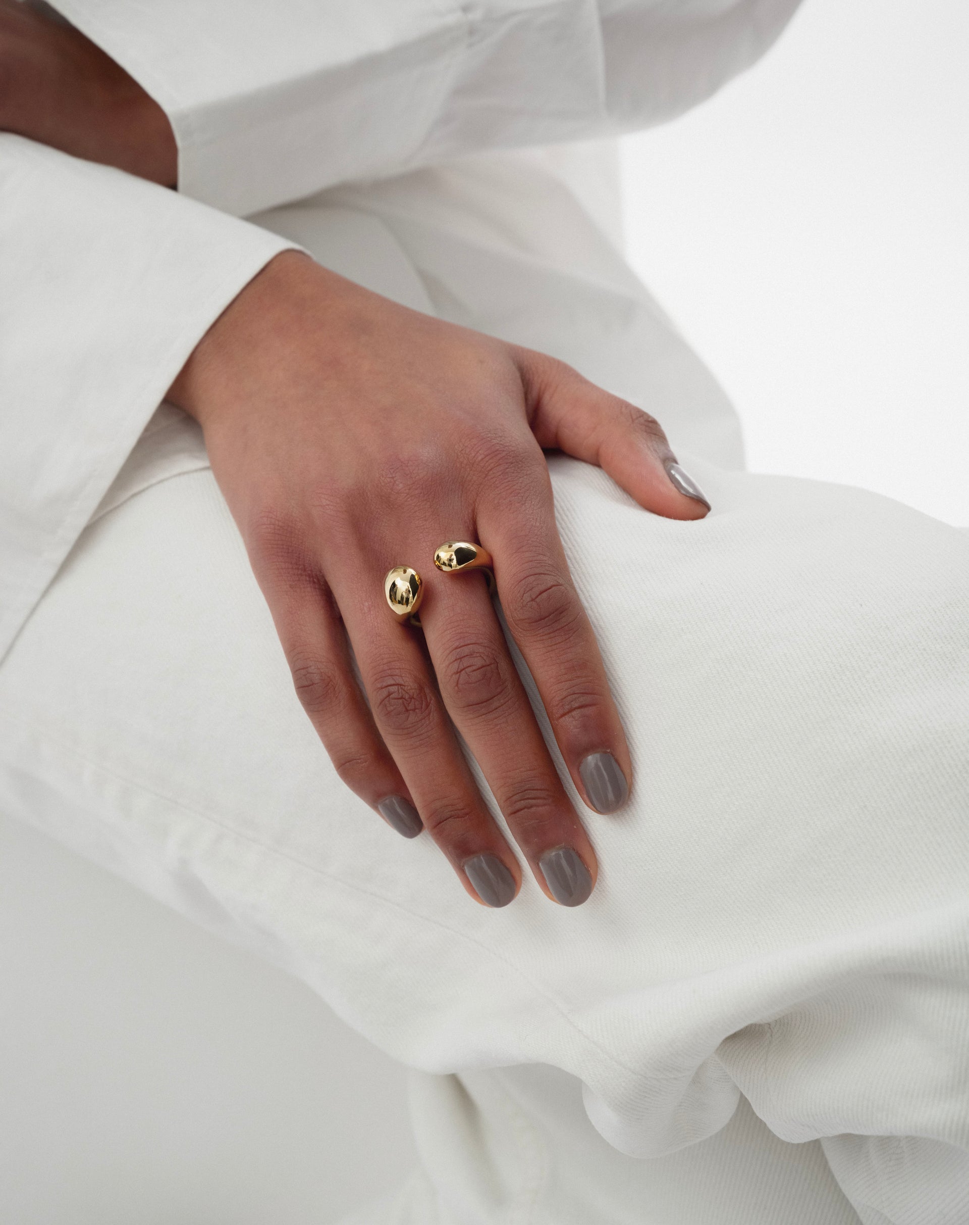 A model shot of the Bolded Drops Ring in gold, worn on a finger to showcase its open design with two smooth, drop-shaped ends.