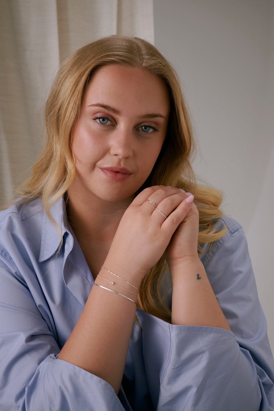 A shot of a model wearing the Tiny Princess Ring in silver, featuring a thin band and a single round, faceted crystal in a princess setting and Tiny Twisted Ring Silver.