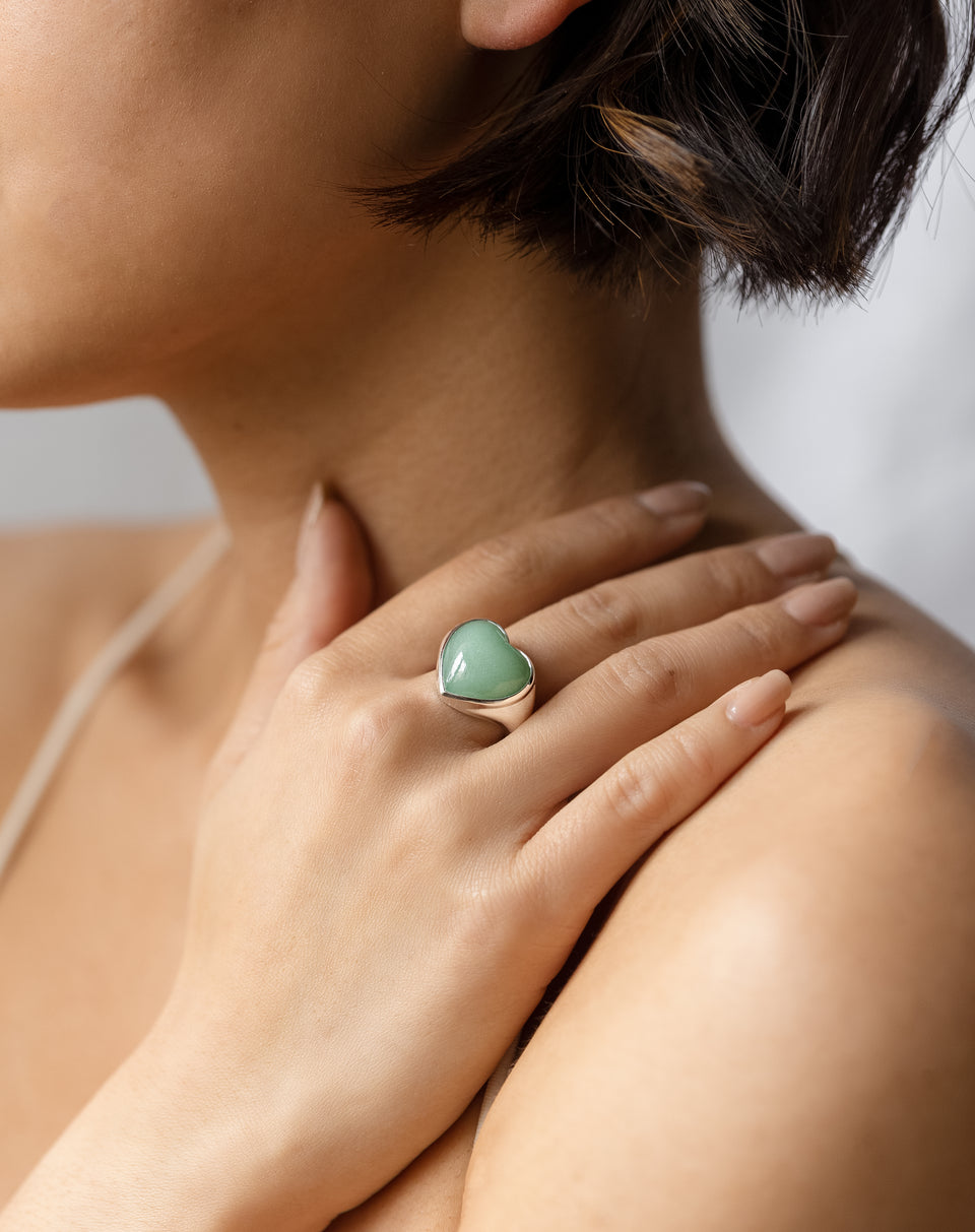 A close-up shot of a model wearing the La La Love Big Heart Ring in silver, featuring a large, heart-shaped green jade stone.
