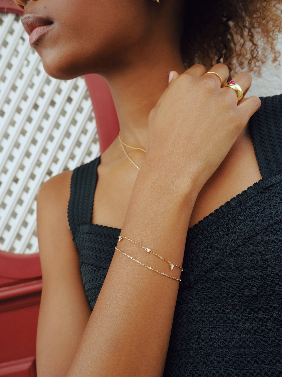 A delicate gold chain bracelet with cubic zirconias layered with a second gold bracelet, paired with a delicate gold necklace, two gold rings, and a small gold hoop earrings.